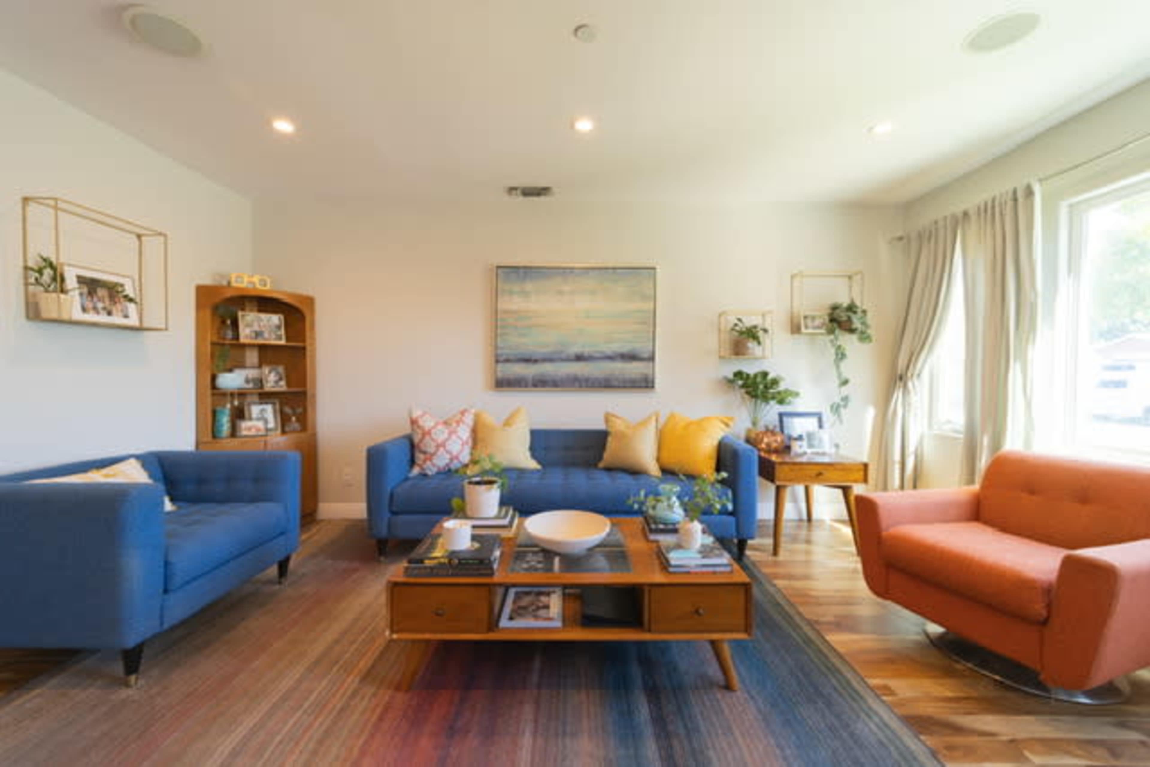 A modern living room features blue and orange sofas, a wooden coffee table, and decorations on the walls and shelves.