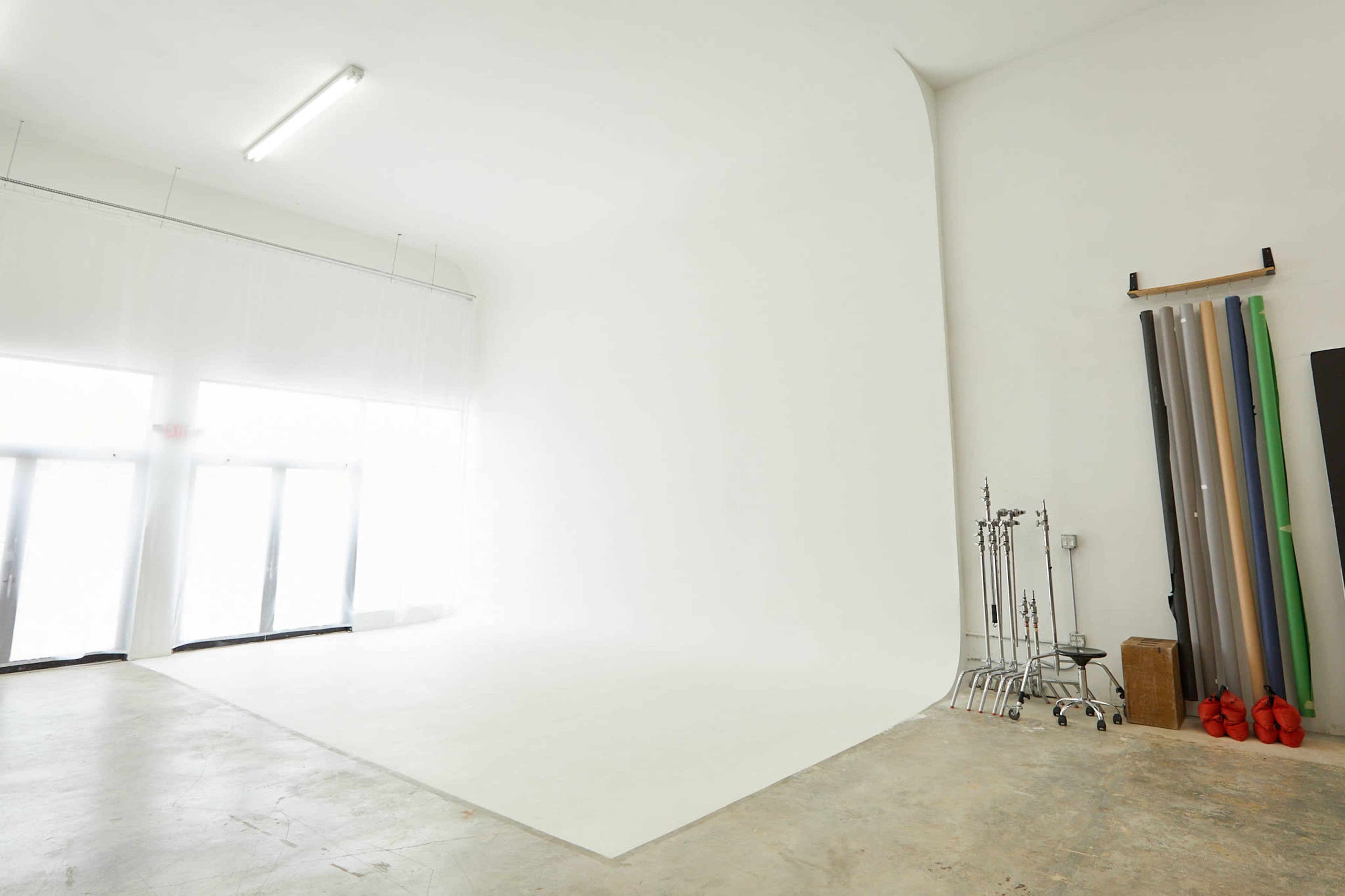 A spacious photography studio with a white backdrop, large windows, and rolls of colored paper on a rack.
