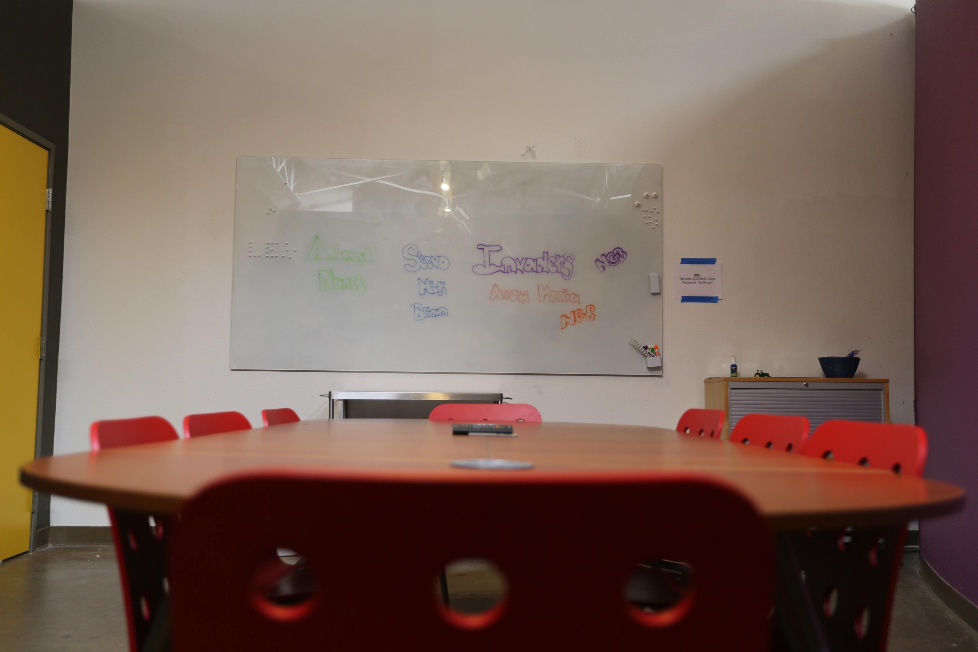 A conference room with a large table surrounded by red chairs and a whiteboard featuring colorful text on one wall.