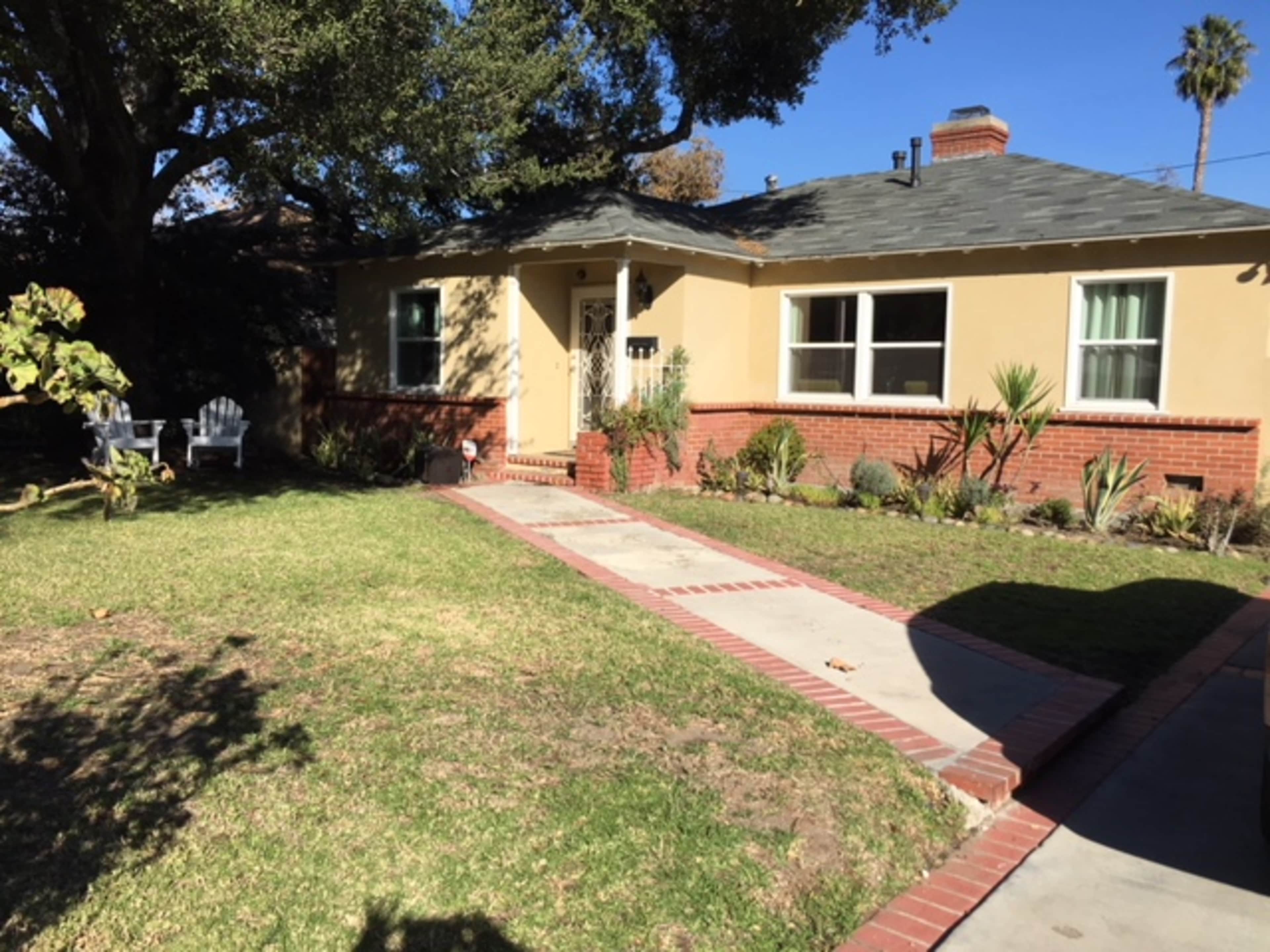 A single-story house with a light-colored exterior and a brick walkway leads to the front door, surrounded by a landscaped yard.