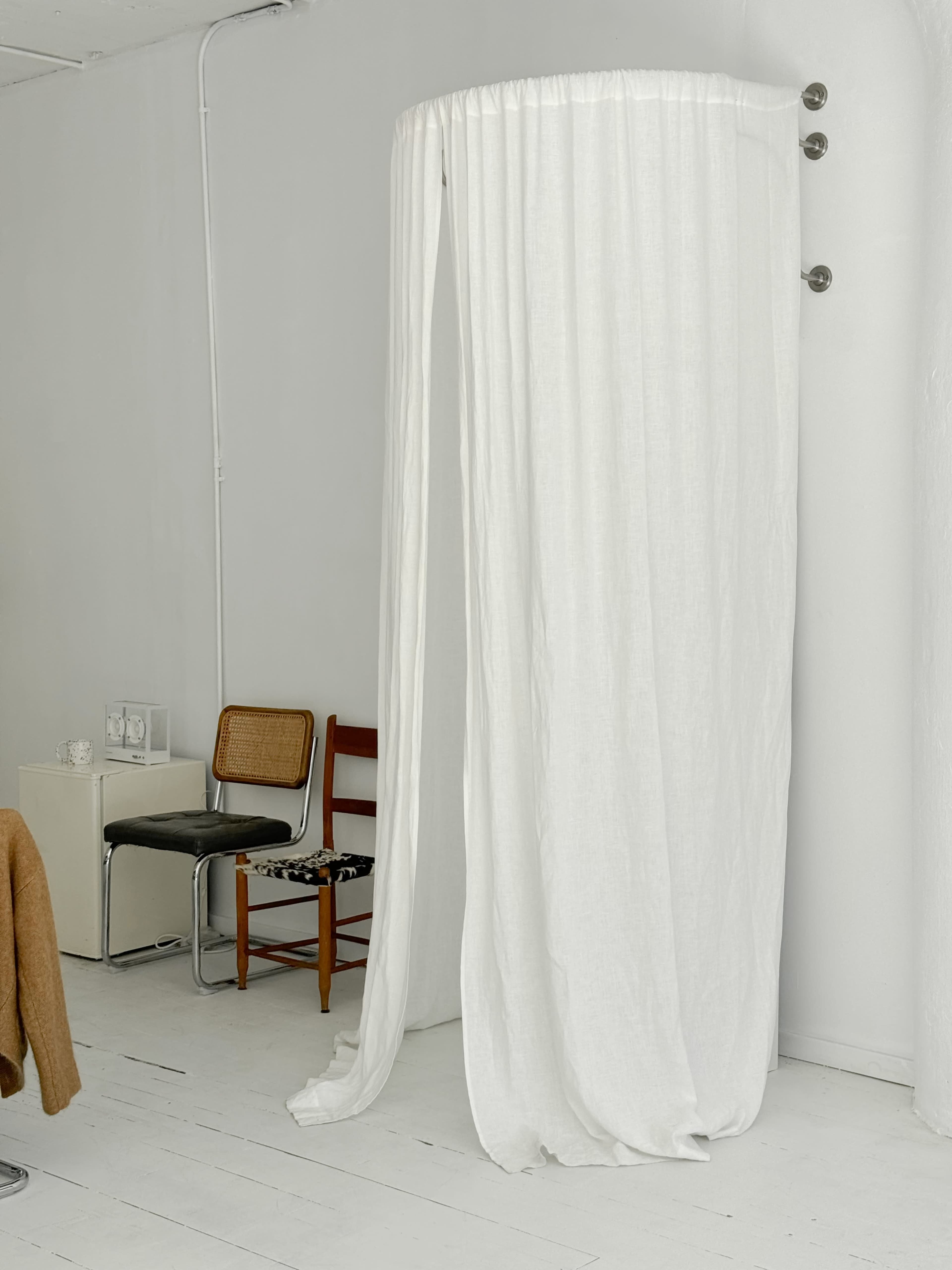 The image features a light-colored, minimalistic room with a white fabric curtain draped around a circular area, alongside two chairs and a small side table.