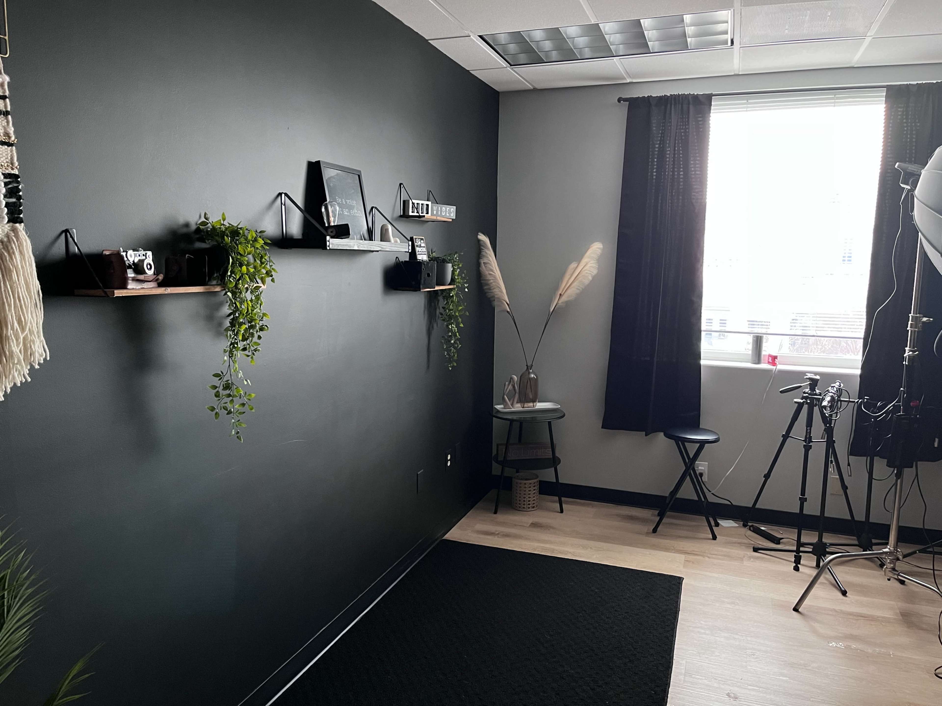 A modern, minimalist room with dark walls, shelves featuring decorative items, a small table with a chair, and a video setup including a tripod.