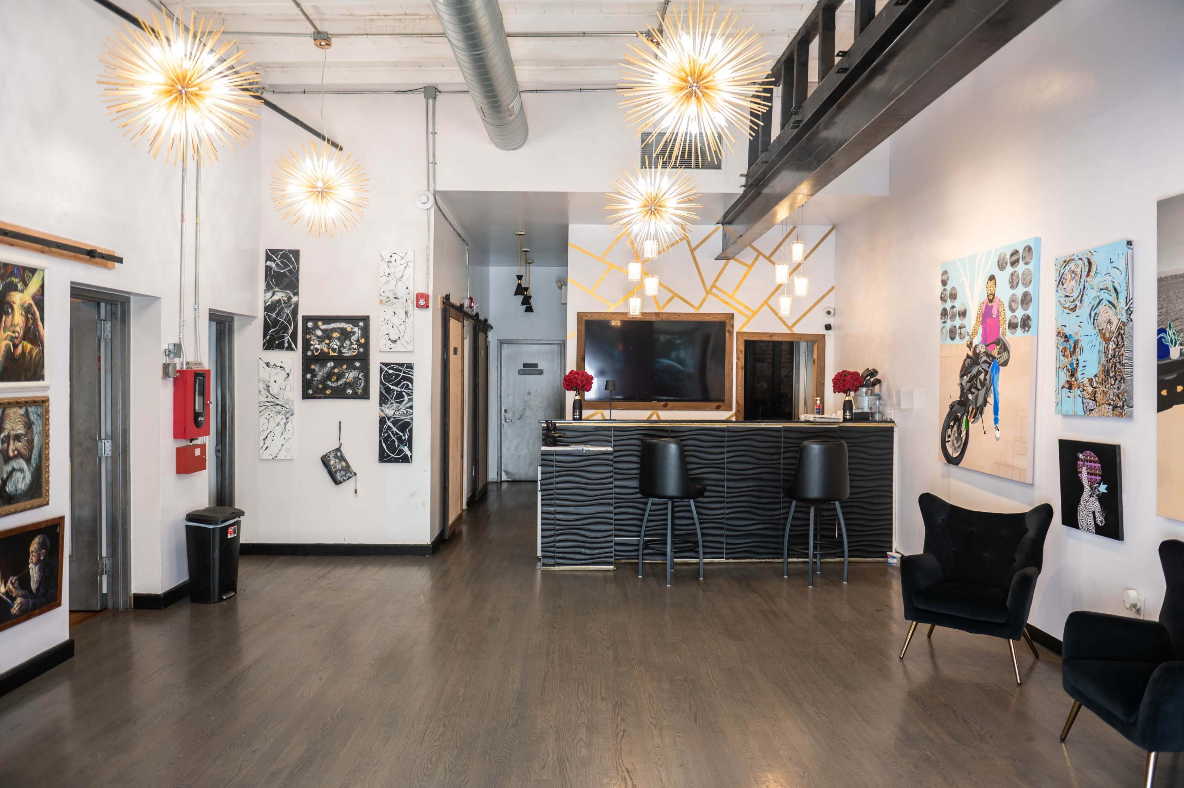 The image shows a modern interior space featuring a bar counter, decorative artwork on the walls, and unique light fixtures.