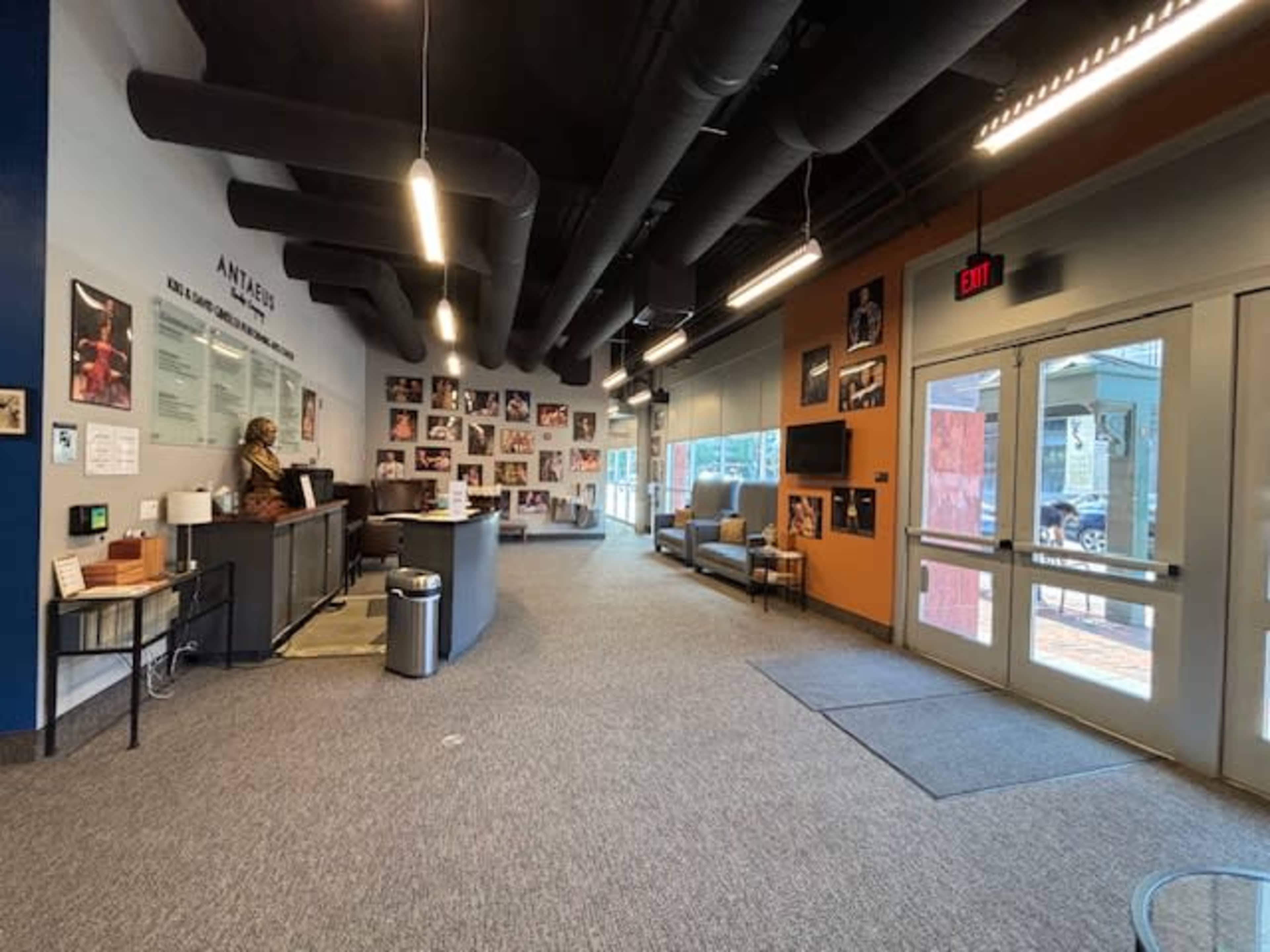 The image shows a spacious lobby area with a reception desk, seating, and walls decorated with photographs.