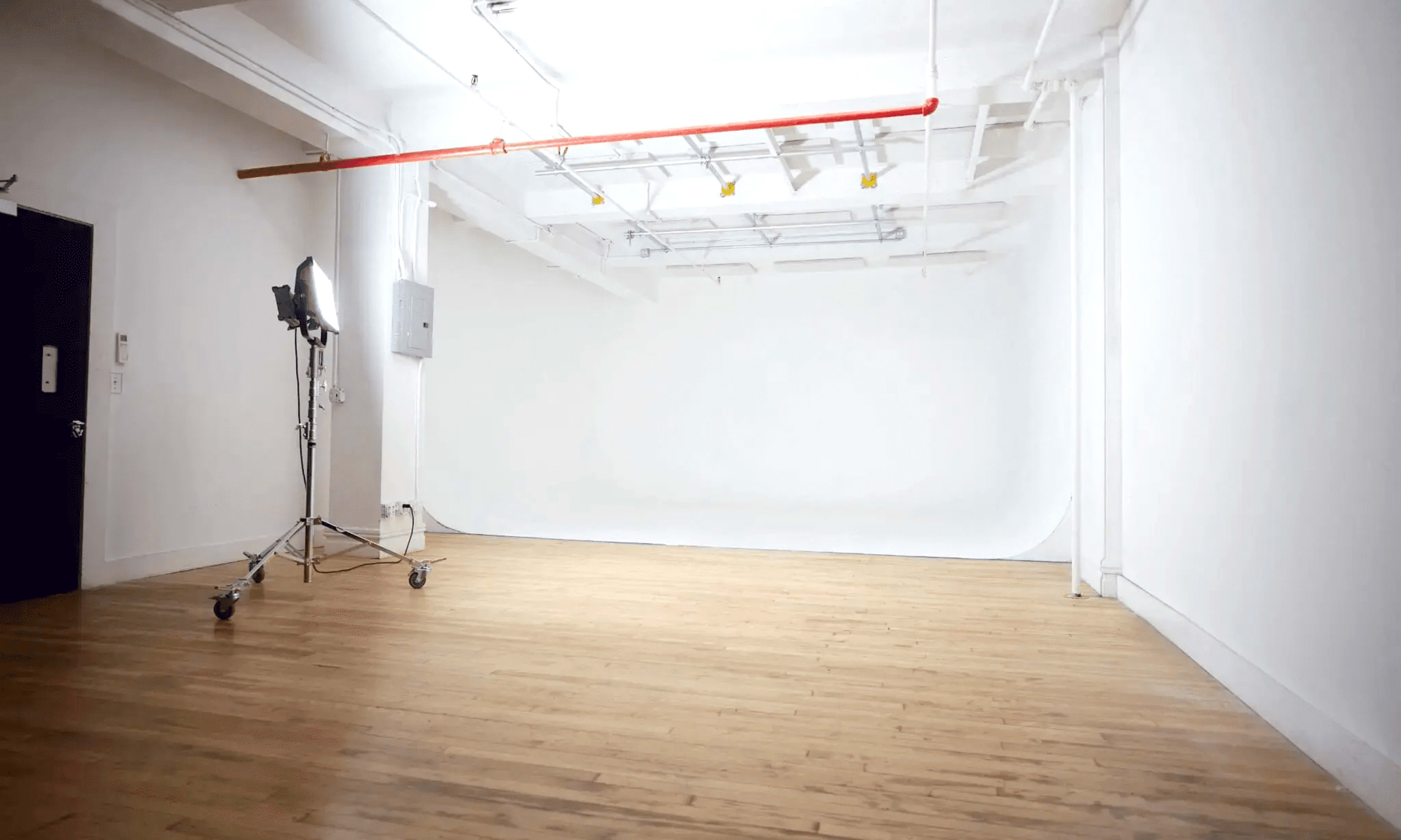 The image shows an empty studio space with a wooden floor and a seamless white backdrop.