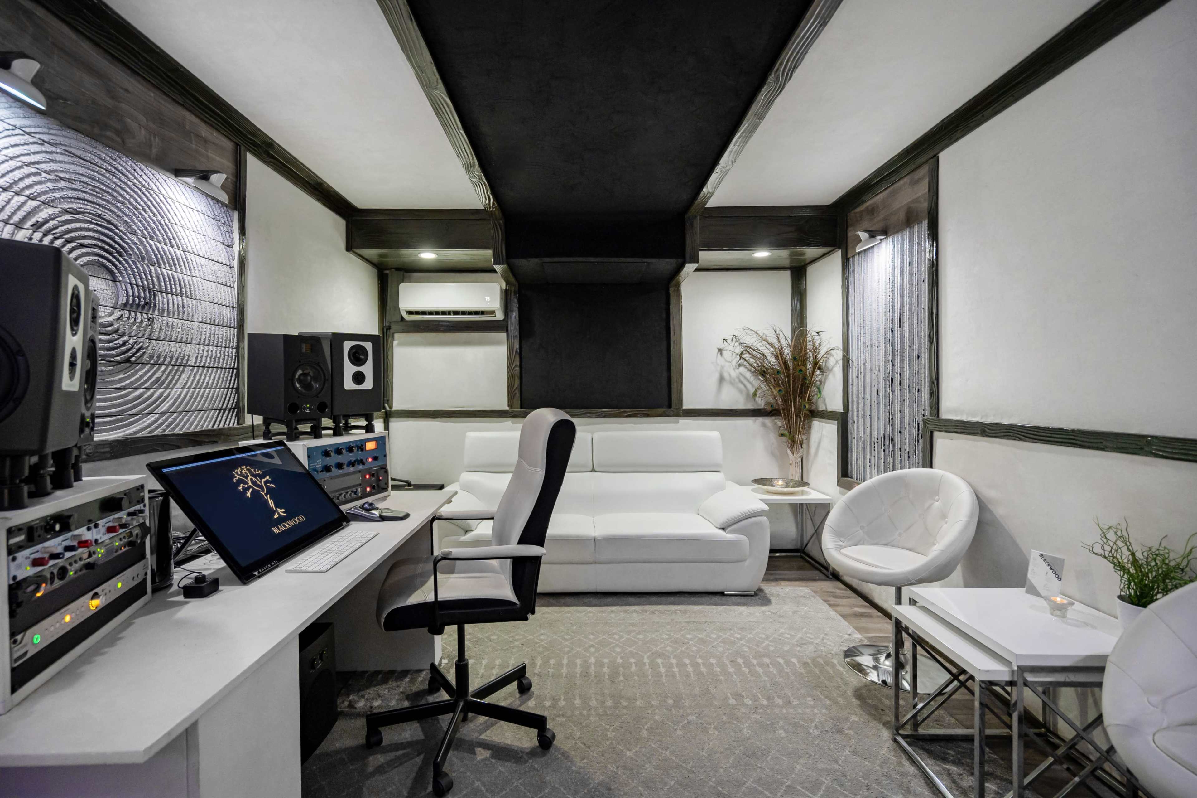 A modern recording studio with a white sofa, audio equipment, and a desk with a computer and office chair.