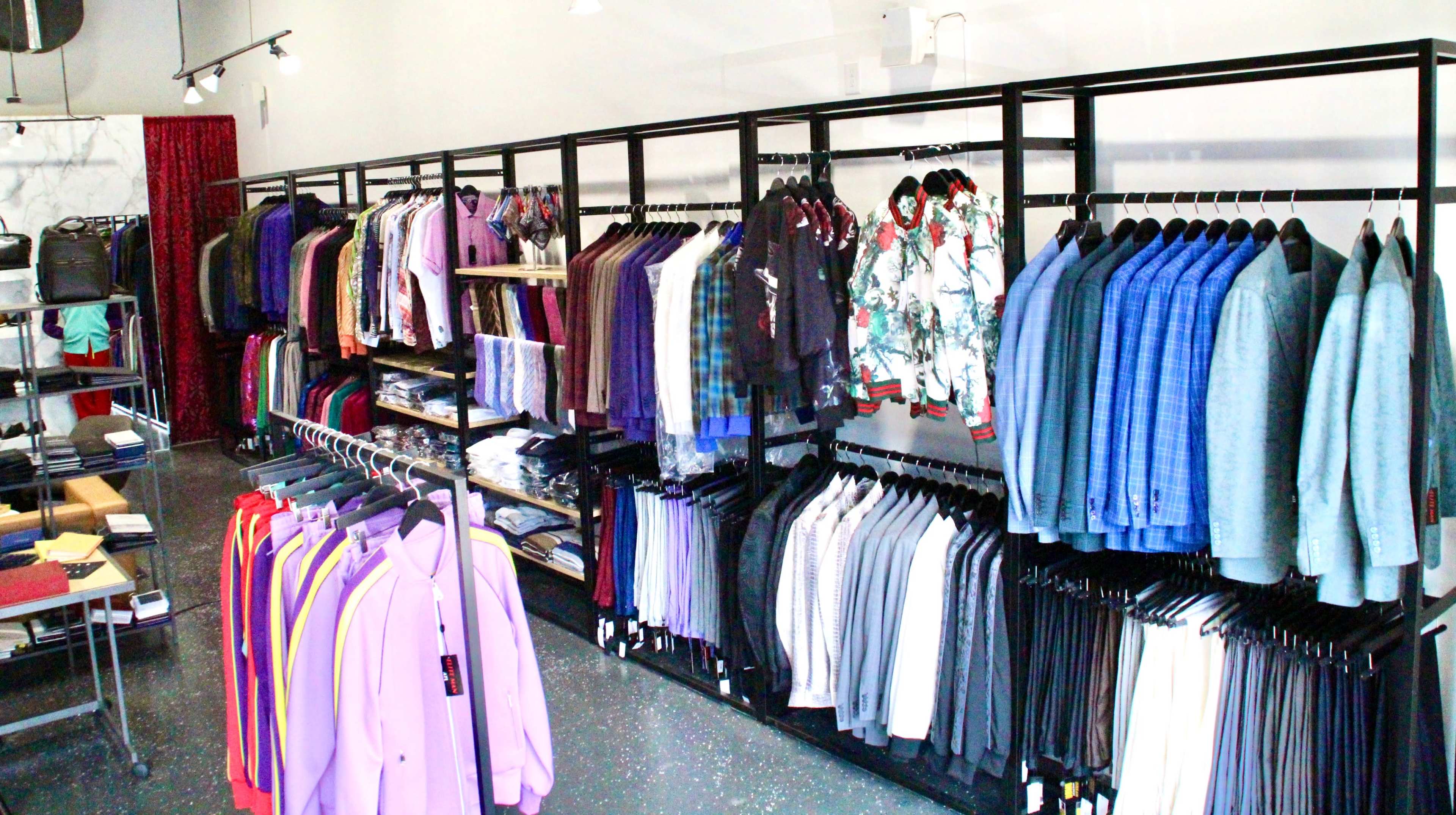 A clothing store displays neatly arranged racks of various shirts, suits, and accessories in a well-lit interior.