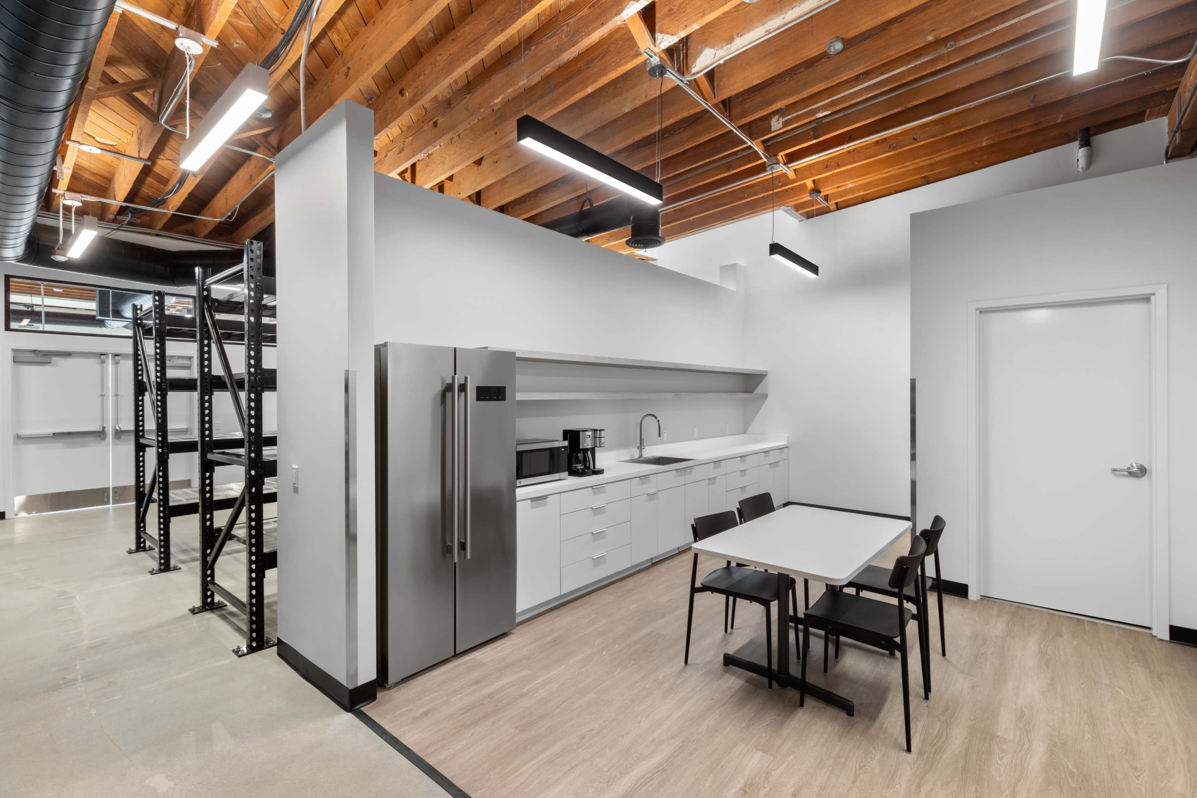 A modern kitchen area with stainless steel appliances, white cabinetry, a dining table, and exposed wooden beams on the ceiling.