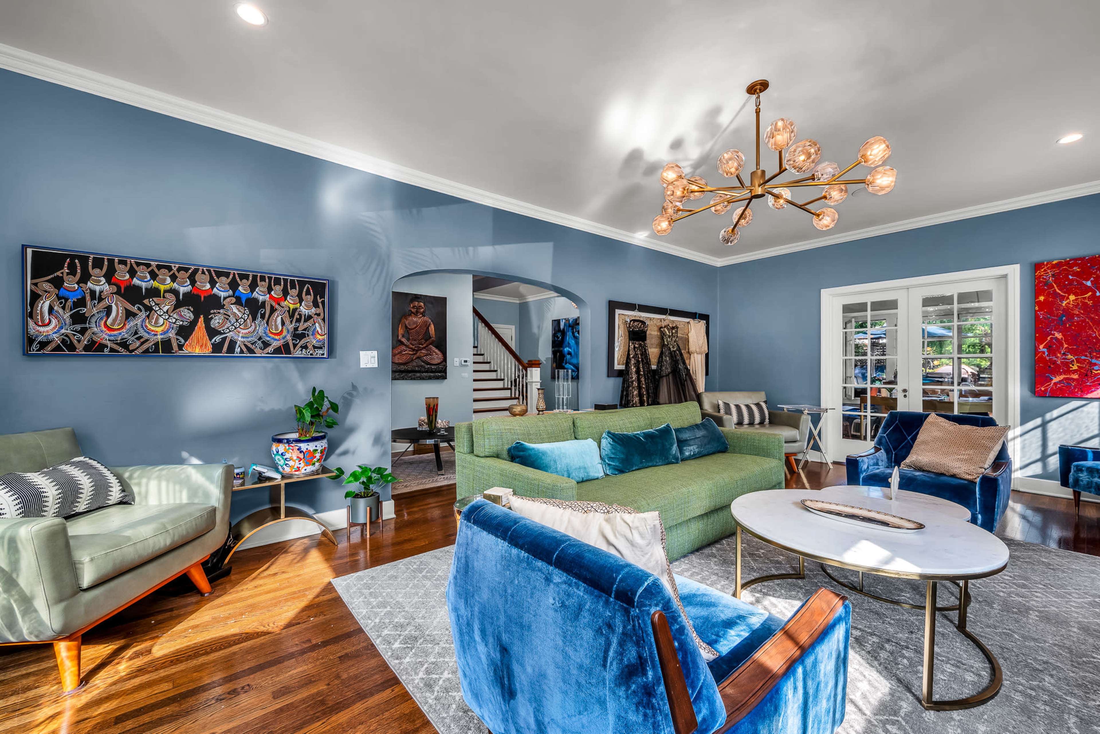 The living room features a mix of contemporary furniture, blue walls, and artistic decor, with ample natural light illuminating the space.