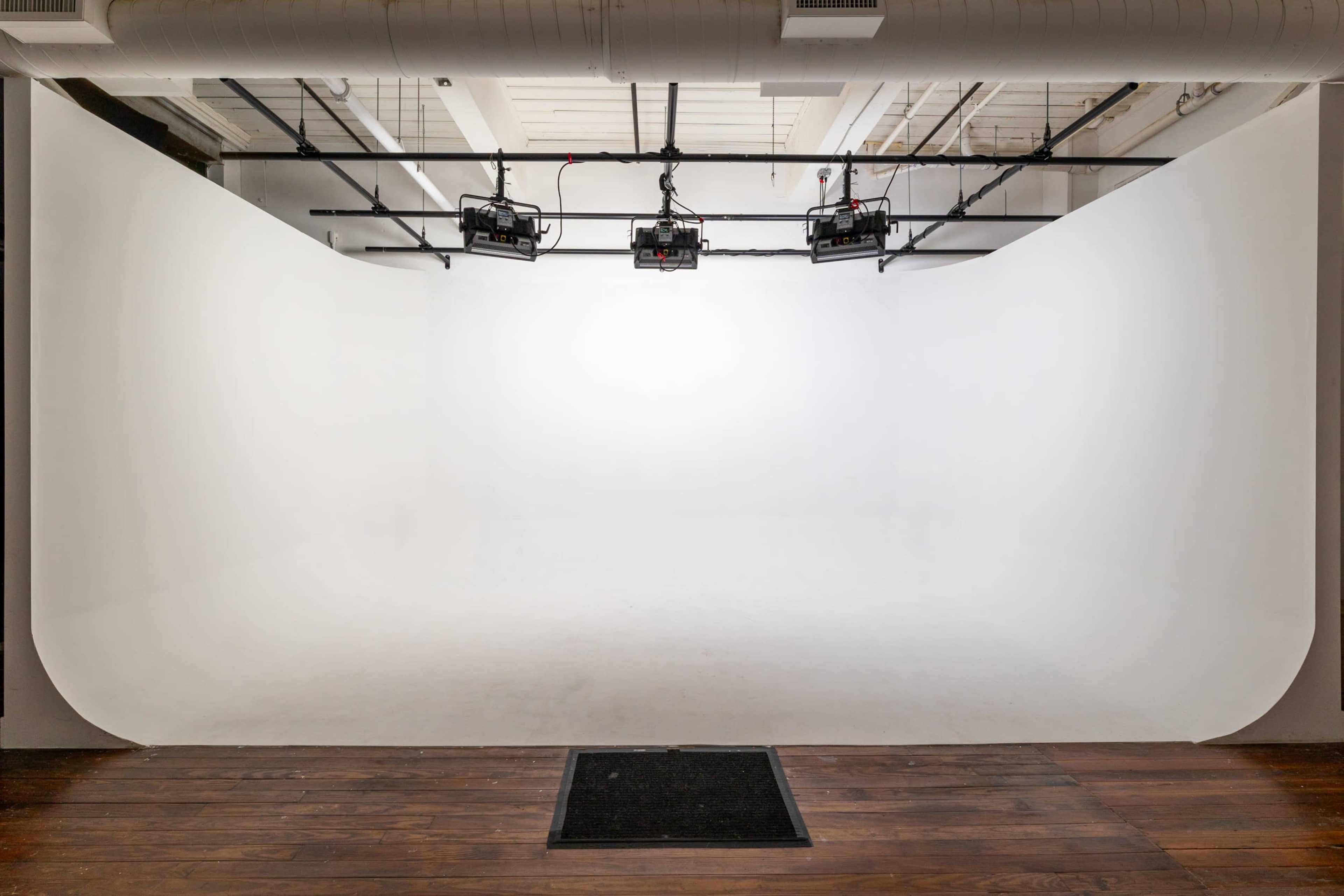 A bright, empty photography studio with a seamless white backdrop and overhead lighting.