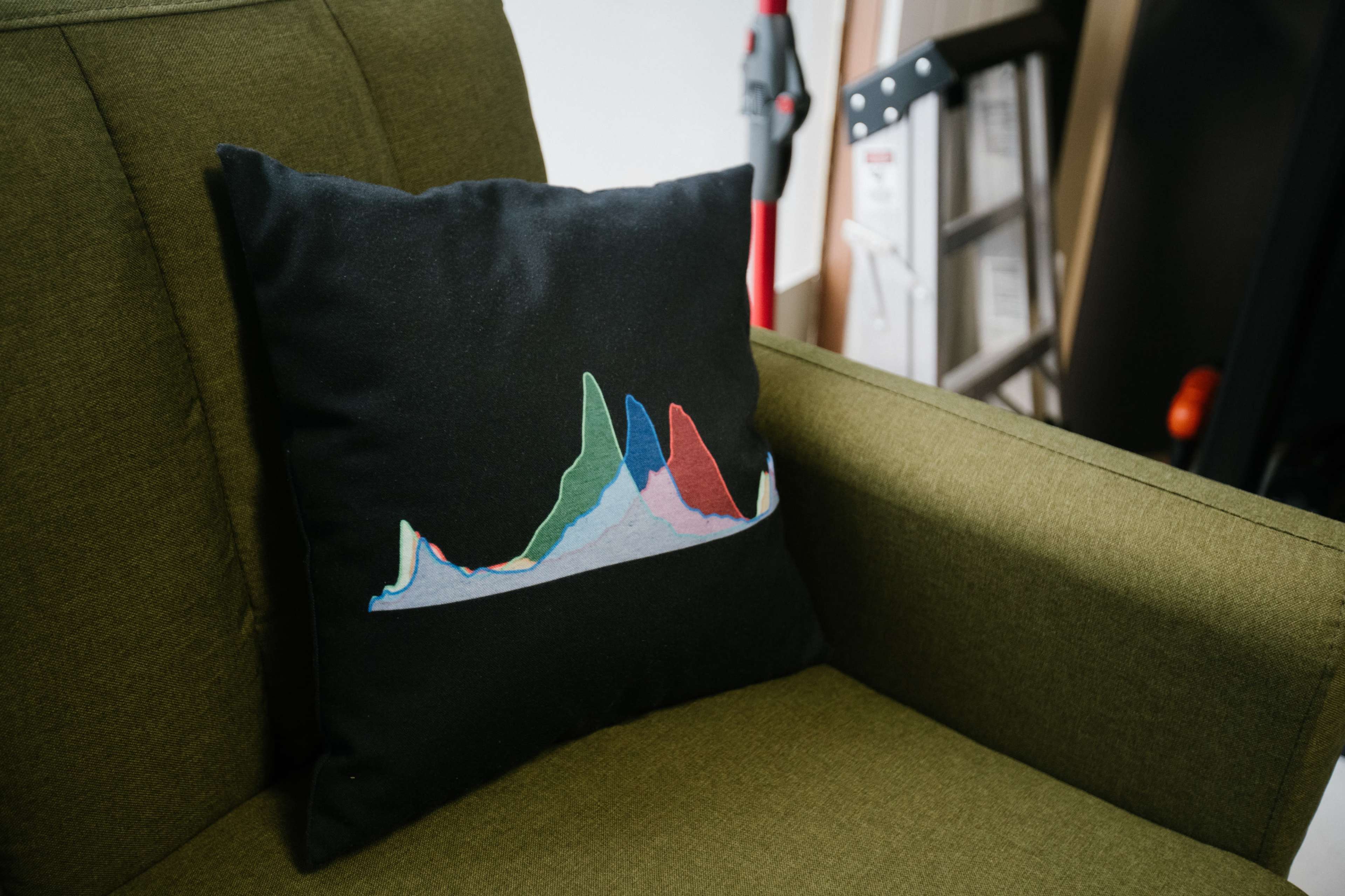 A decorative pillow with a colorful mountain range design is placed on a green armchair.