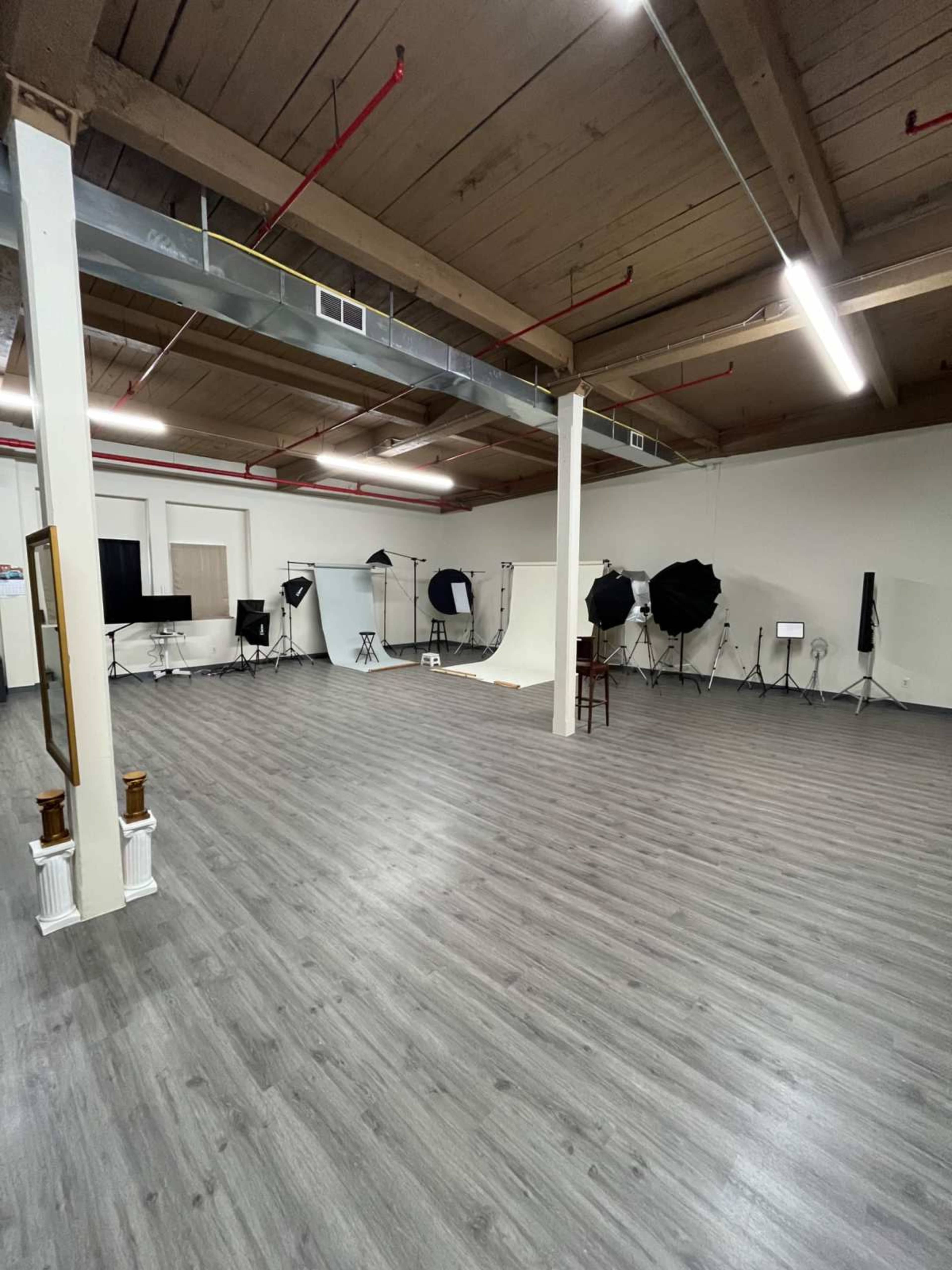 The image shows a spacious photography studio with several lighting setups and backdrops arranged around the room.