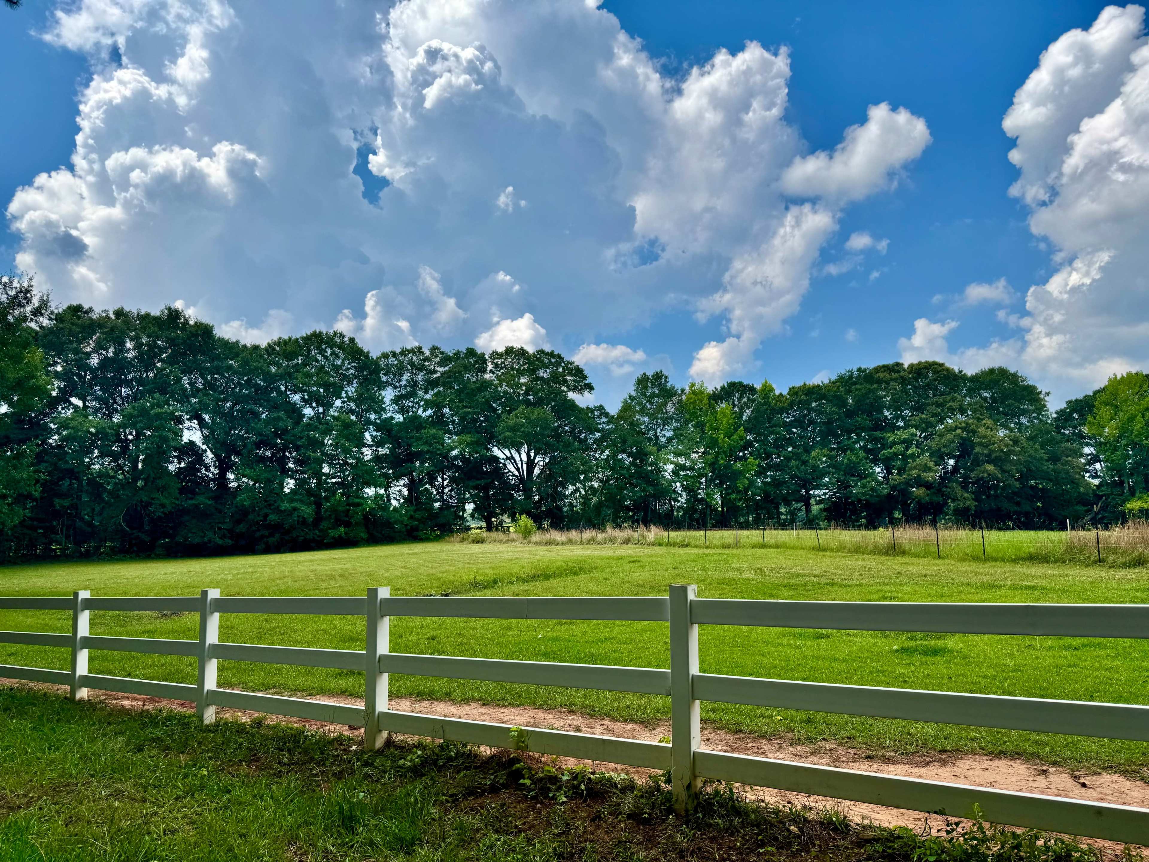 A white fence borders a lush green field under a partly cloudy sky.