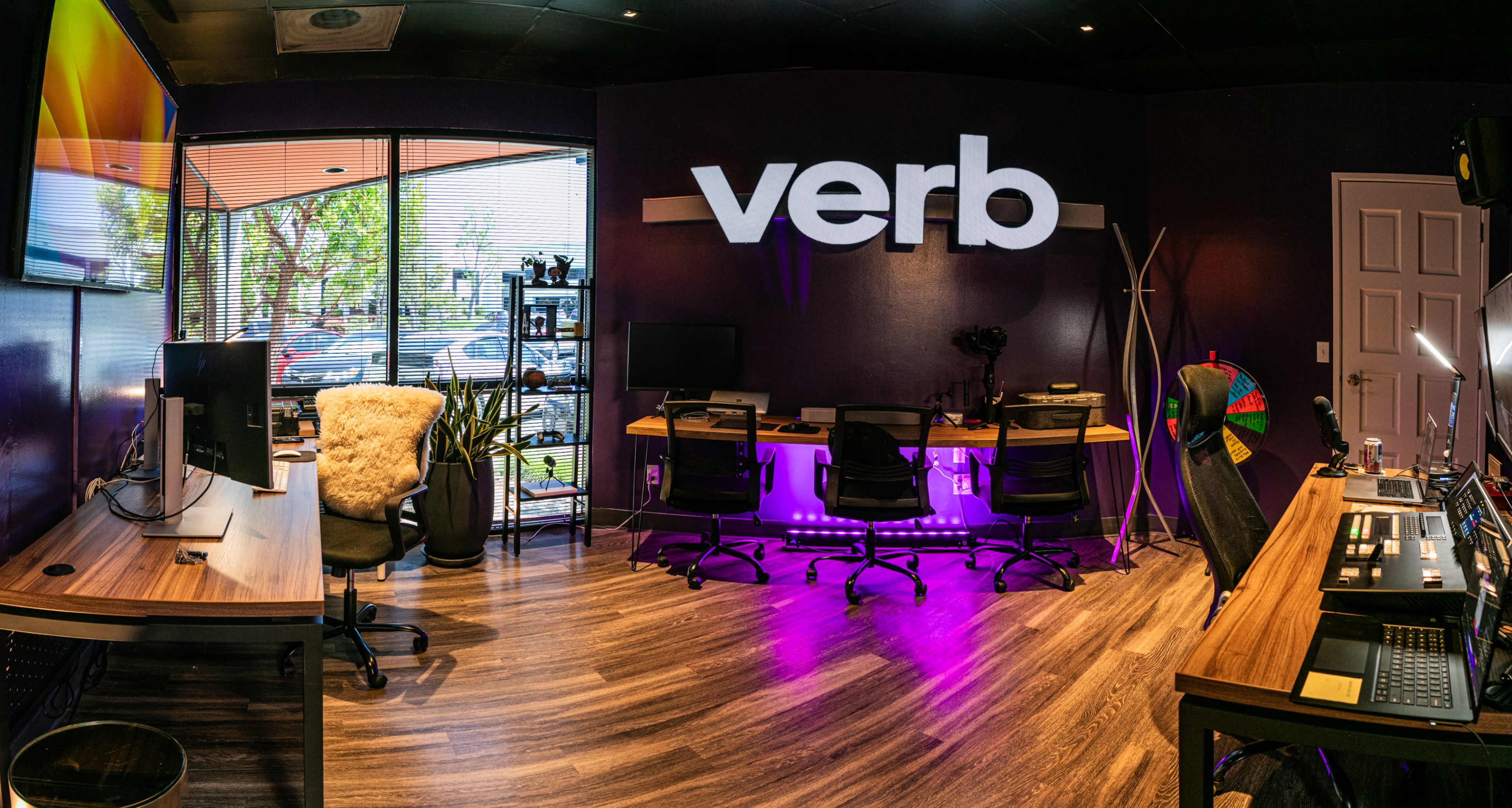 A modern office space with a prominent "verb" sign, multiple workstations equipped with computers, and an inviting atmosphere created by purple lighting.