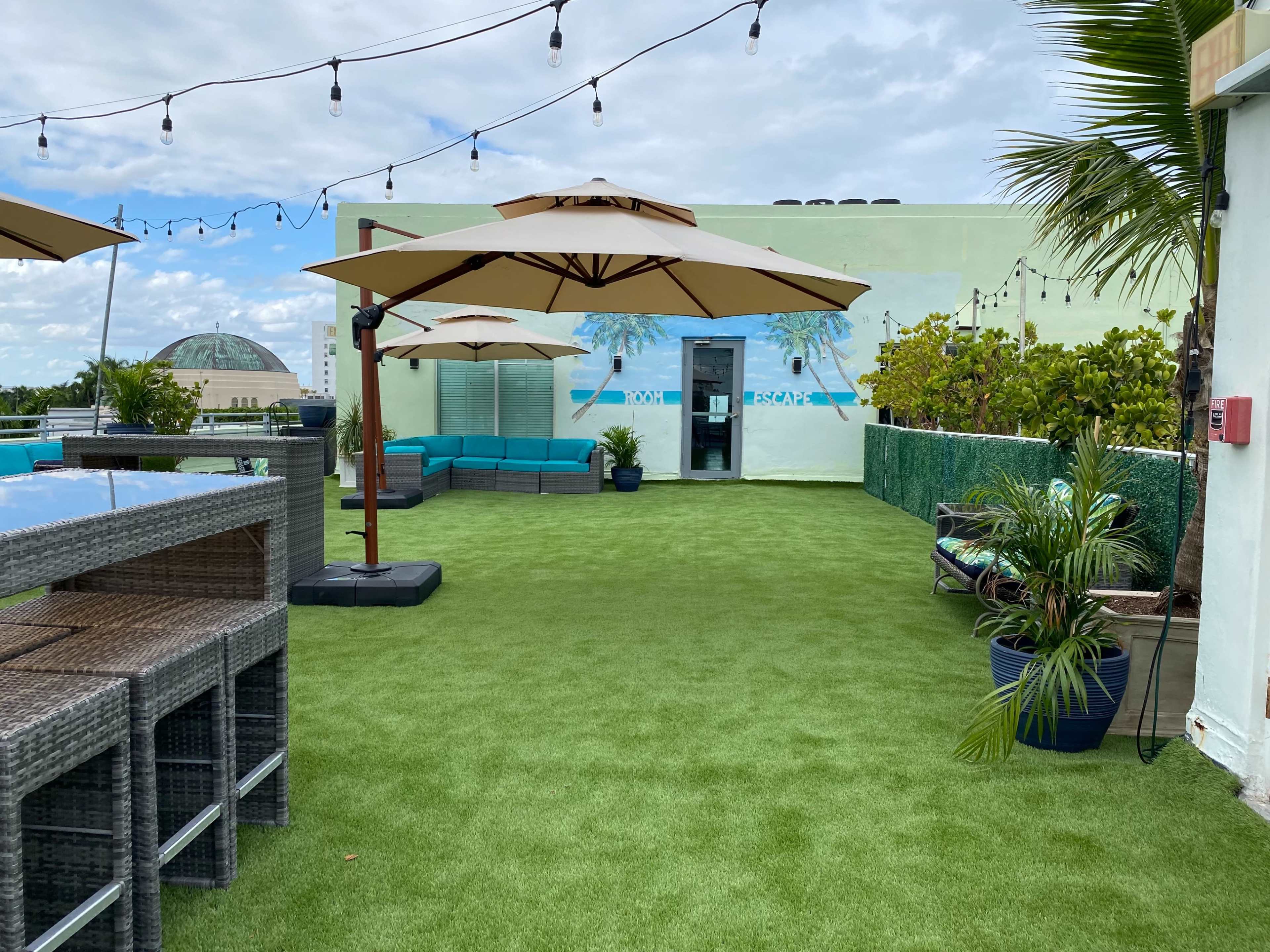 The rooftop area features synthetic grass, lounge seating with umbrellas, and potted plants against a colorful mural backdrop.