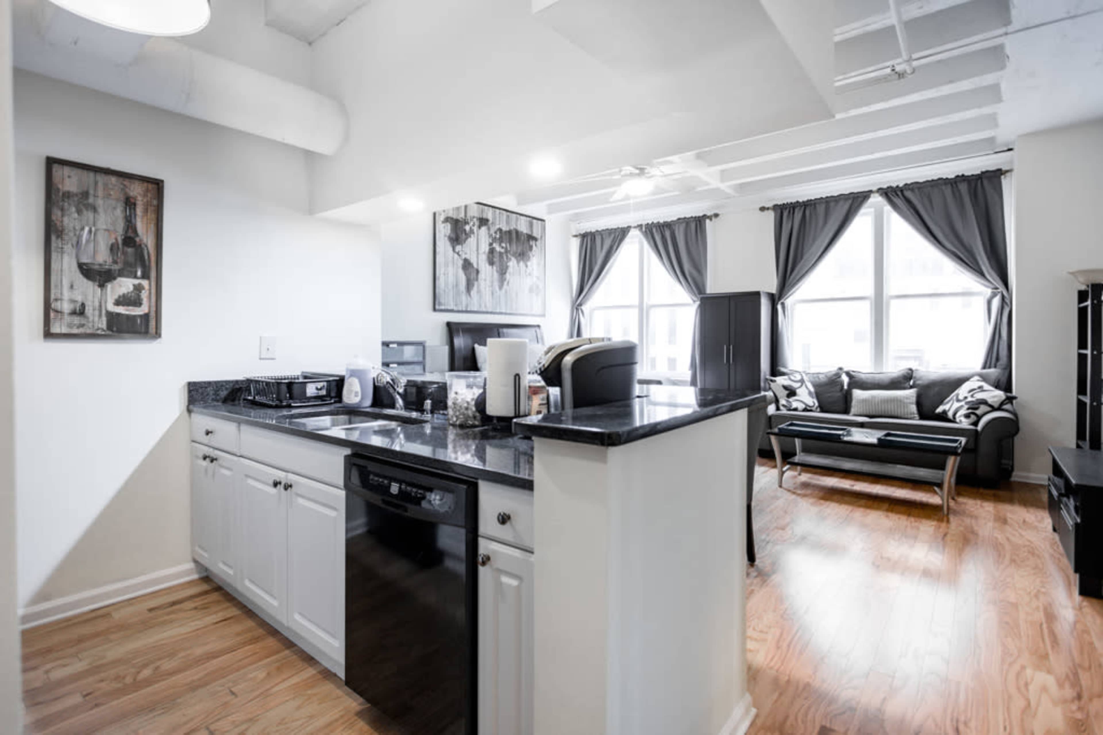 A modern kitchen and living area with a granite countertop, appliances, and large windows adorned with dark curtains.