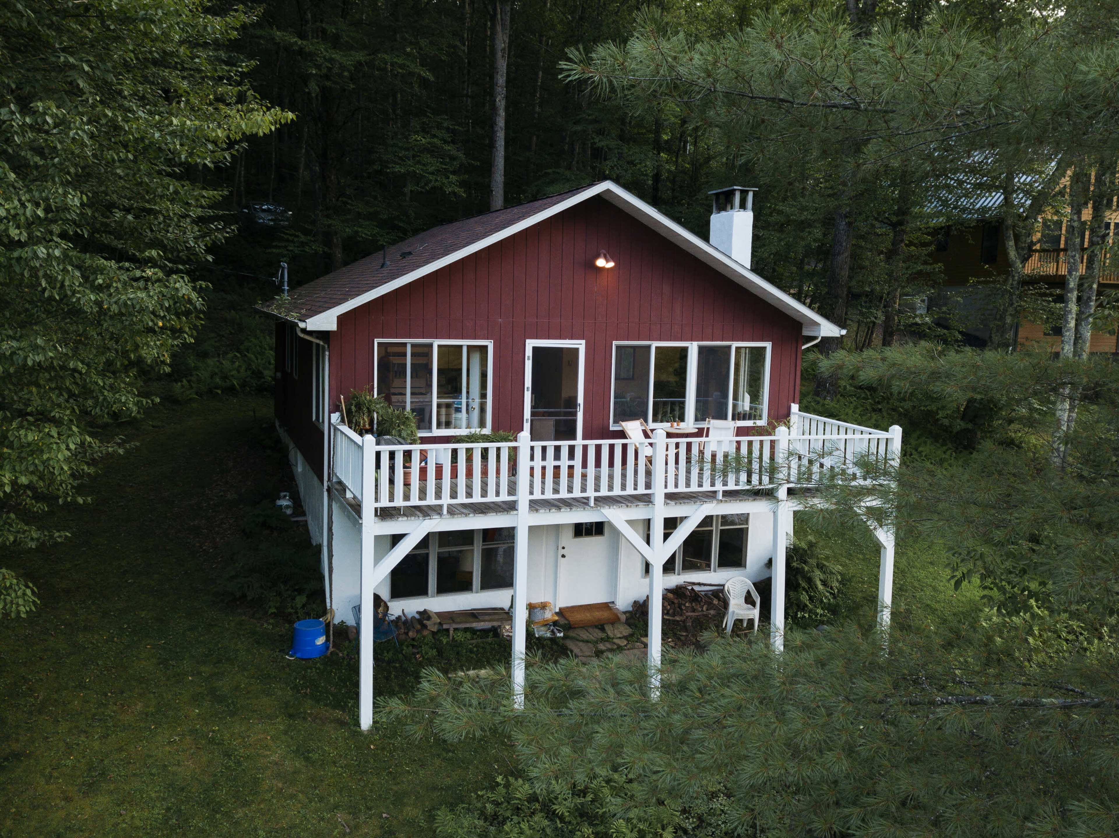 A two-story red house with a white balcony is surrounded by dense trees and greenery.