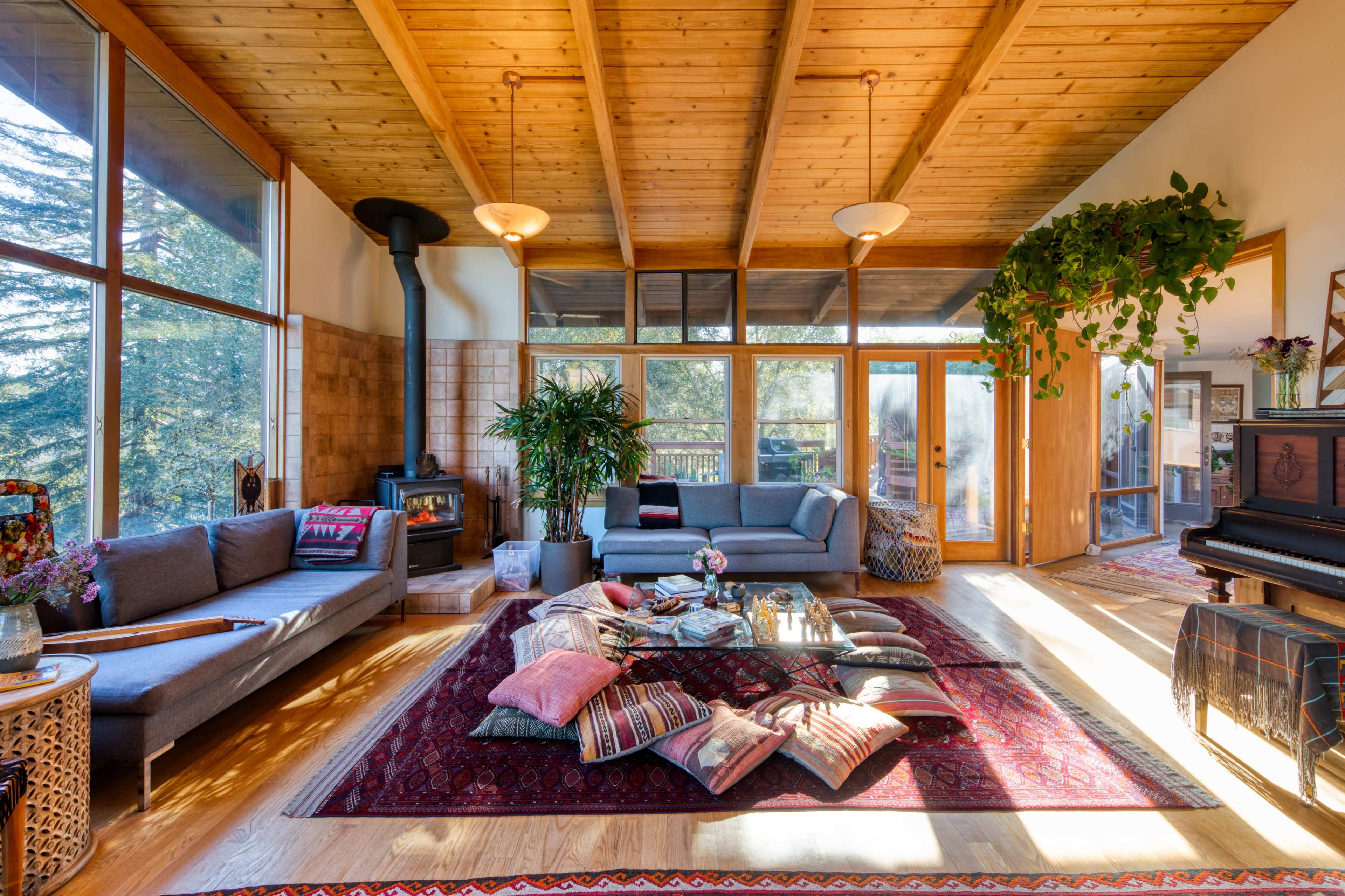 A spacious living room features a vaulted wooden ceiling, a fireplace, and a central area adorned with a rug and various cushions.