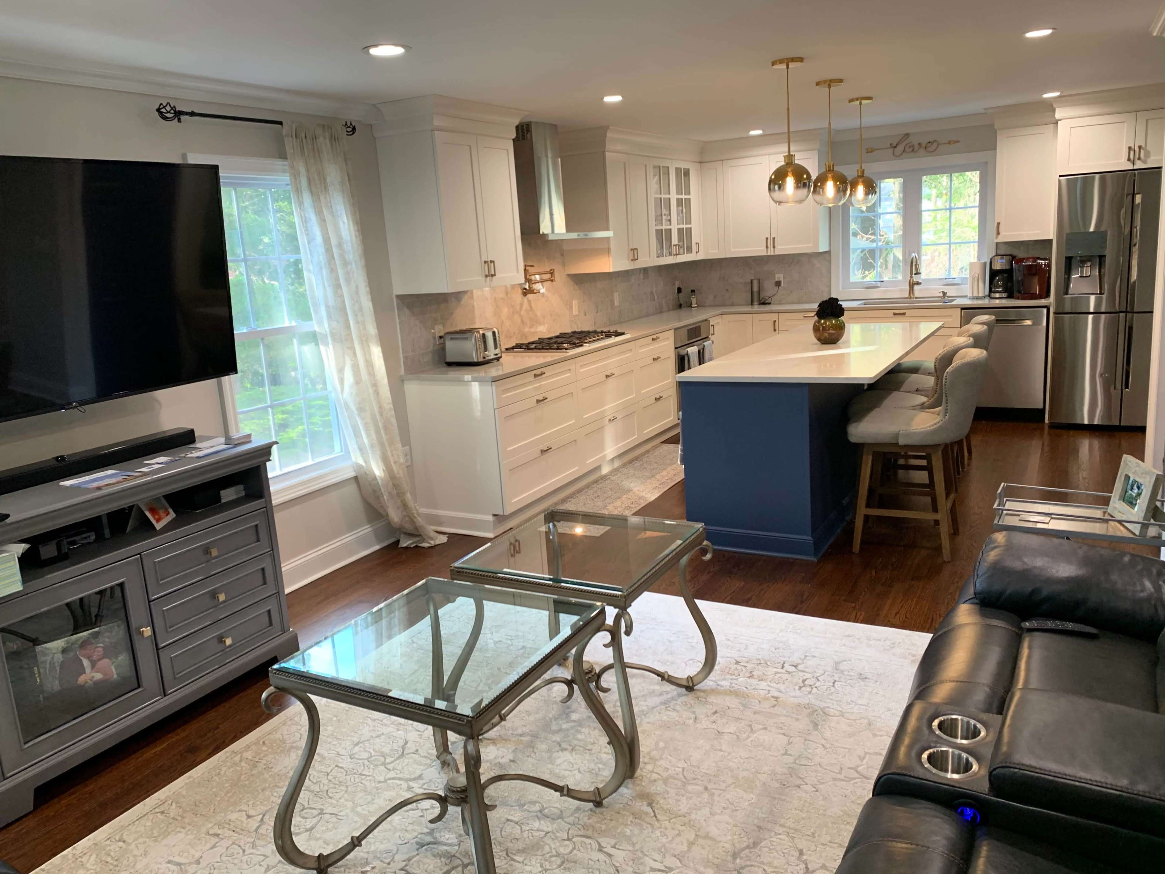 A modern kitchen and living area featuring white cabinetry, stainless steel appliances, a large island with seating, and a glass coffee table on a patterned rug.