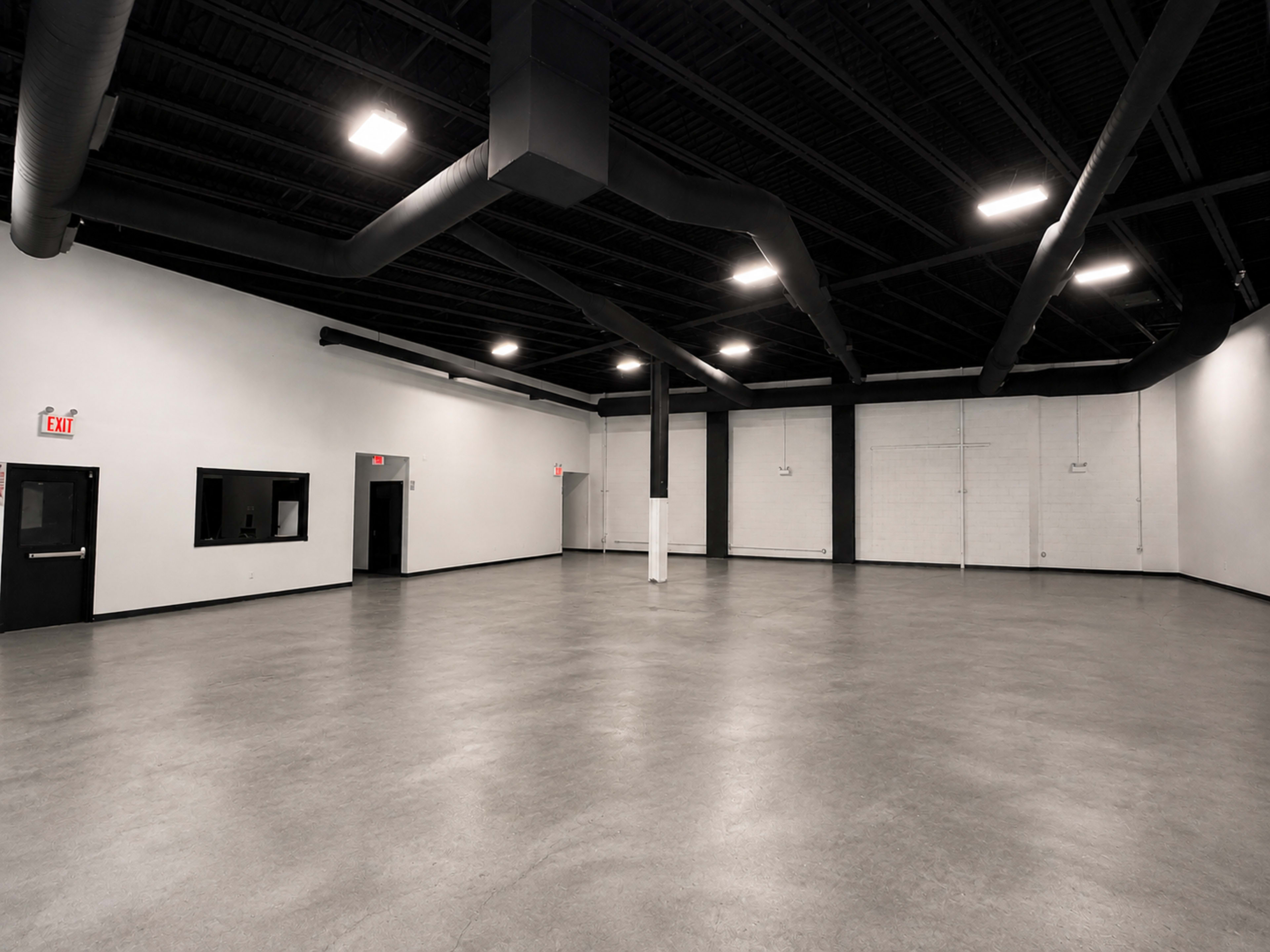 The image shows an empty room with a polished concrete floor, black ceiling, and several exits along the walls.