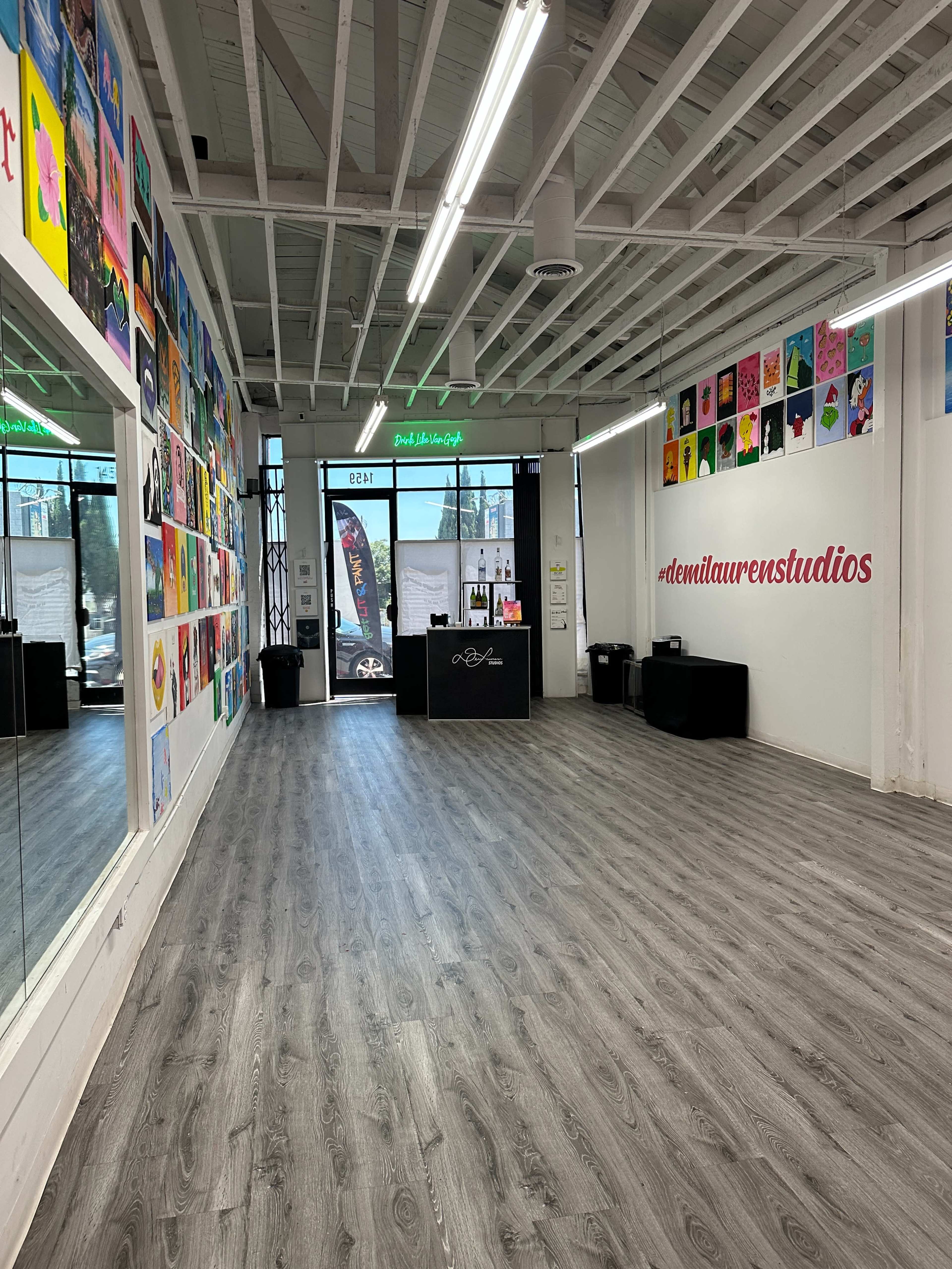 A spacious art studio with a mirrored wall, colorful artworks displayed on one side, and a reception area featuring a desk and signage.