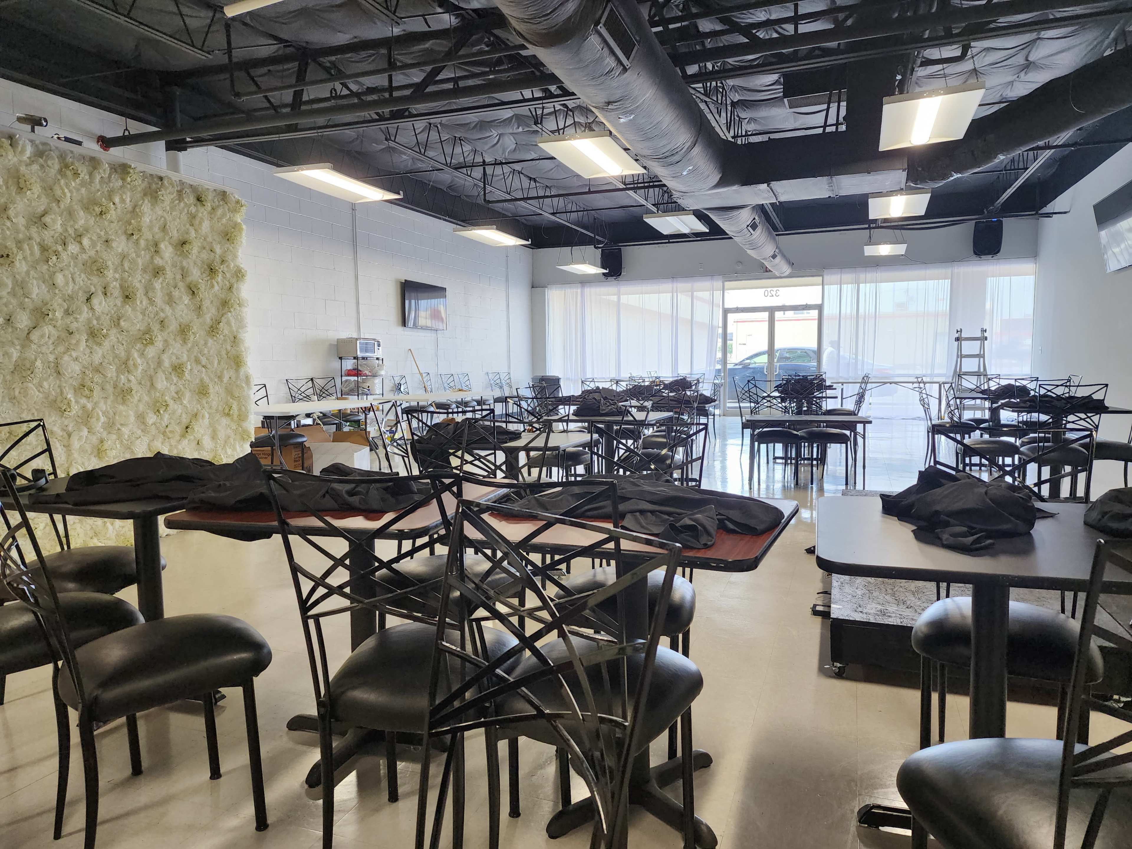 An empty dining area with black tables and chairs arranged neatly, facing a wall adorned with a decorative floral installation.
