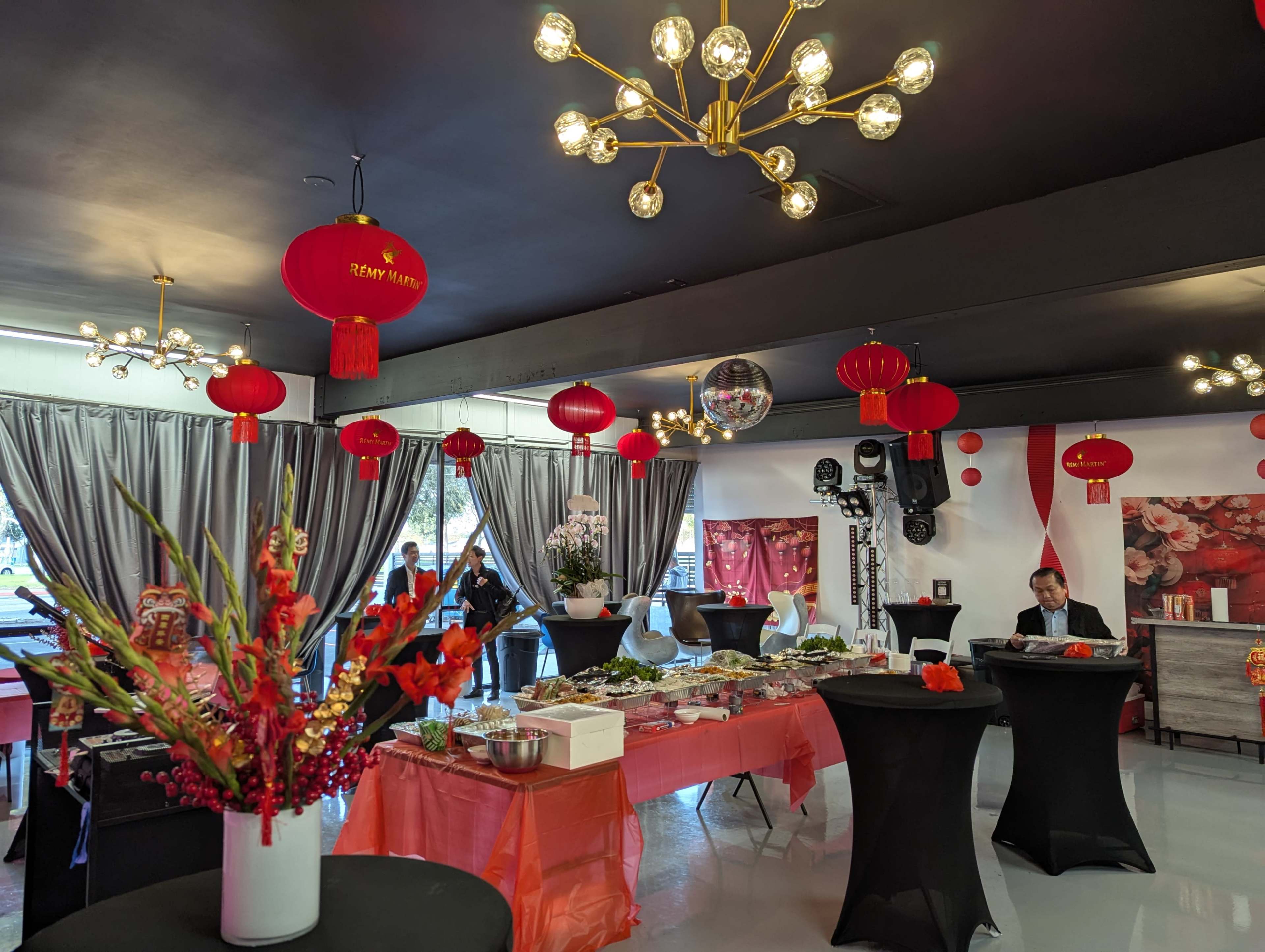 The scene features a well-decorated event space with tables set for a celebration, red lanterns hanging from the ceiling, and food arranged on several tables.