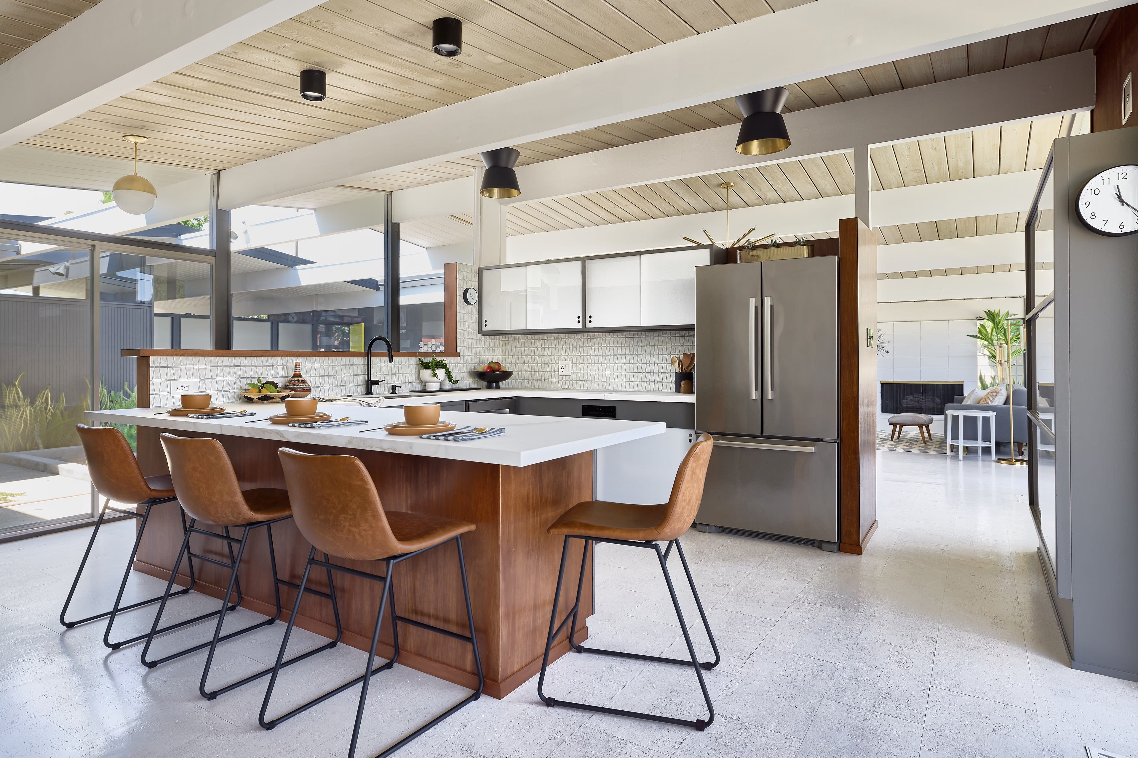 A modern kitchen with a central island, four bar stools, and large windows that illuminate the space.
