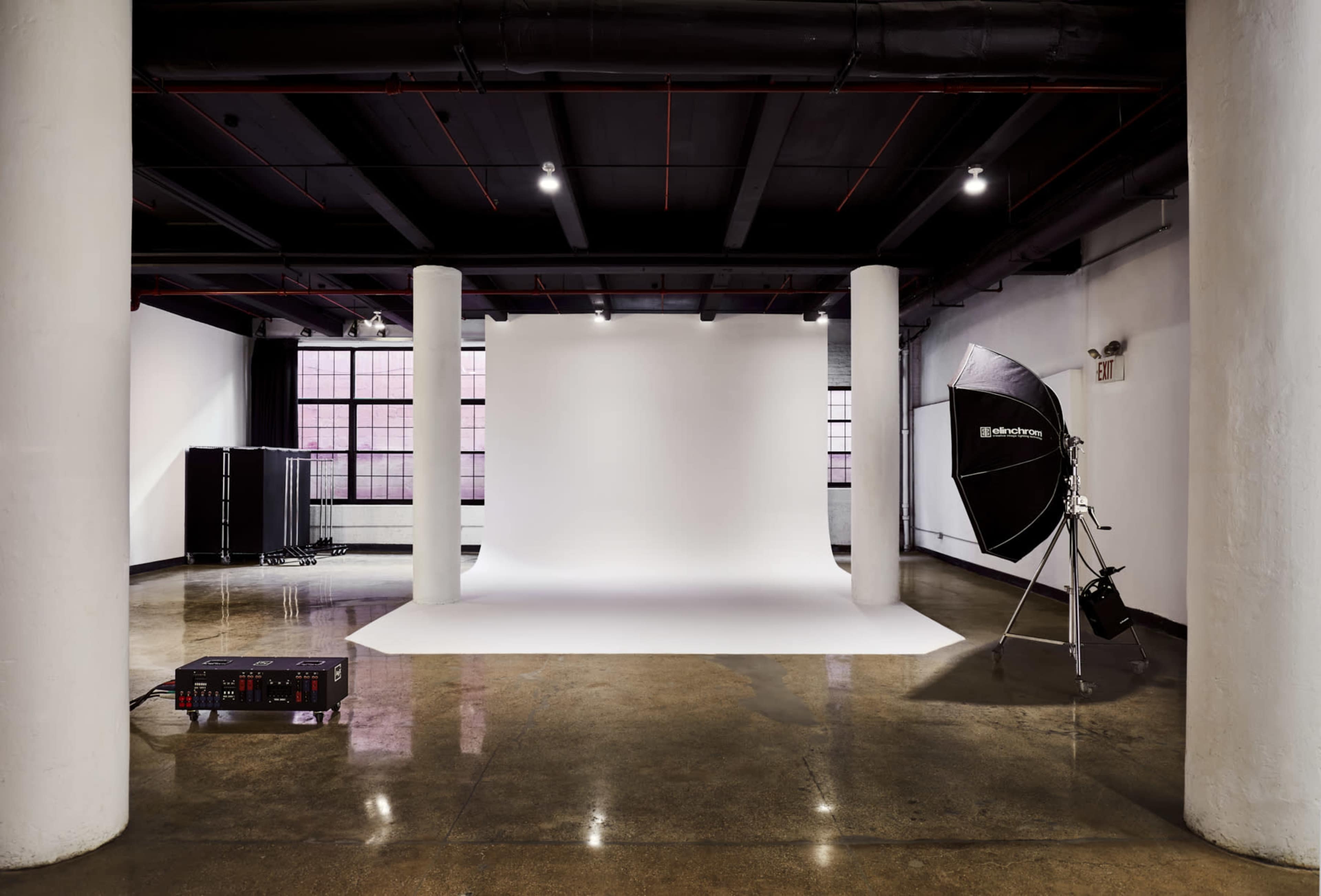 The image shows a photography studio featuring a white backdrop, studio lights, and polished concrete floors.