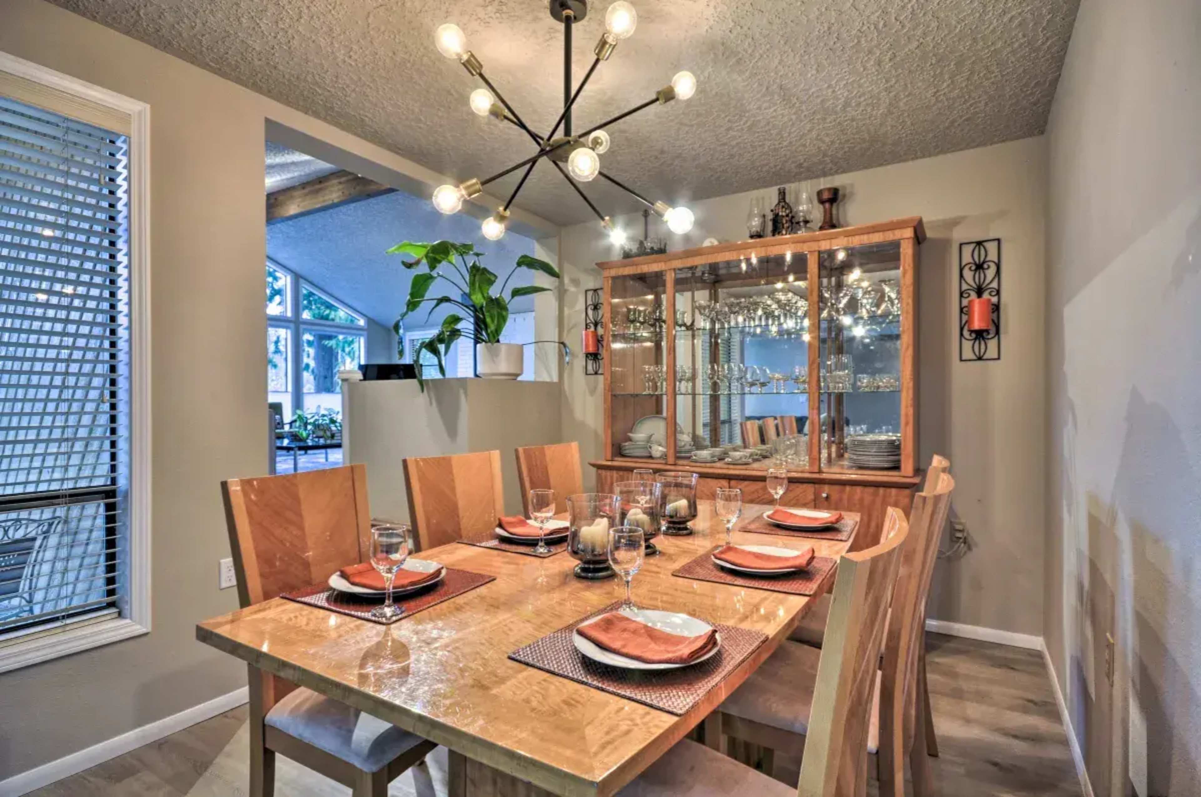 A modern dining room features a wooden table set for dinner with eight chairs, surrounded by glassware and a display cabinet.