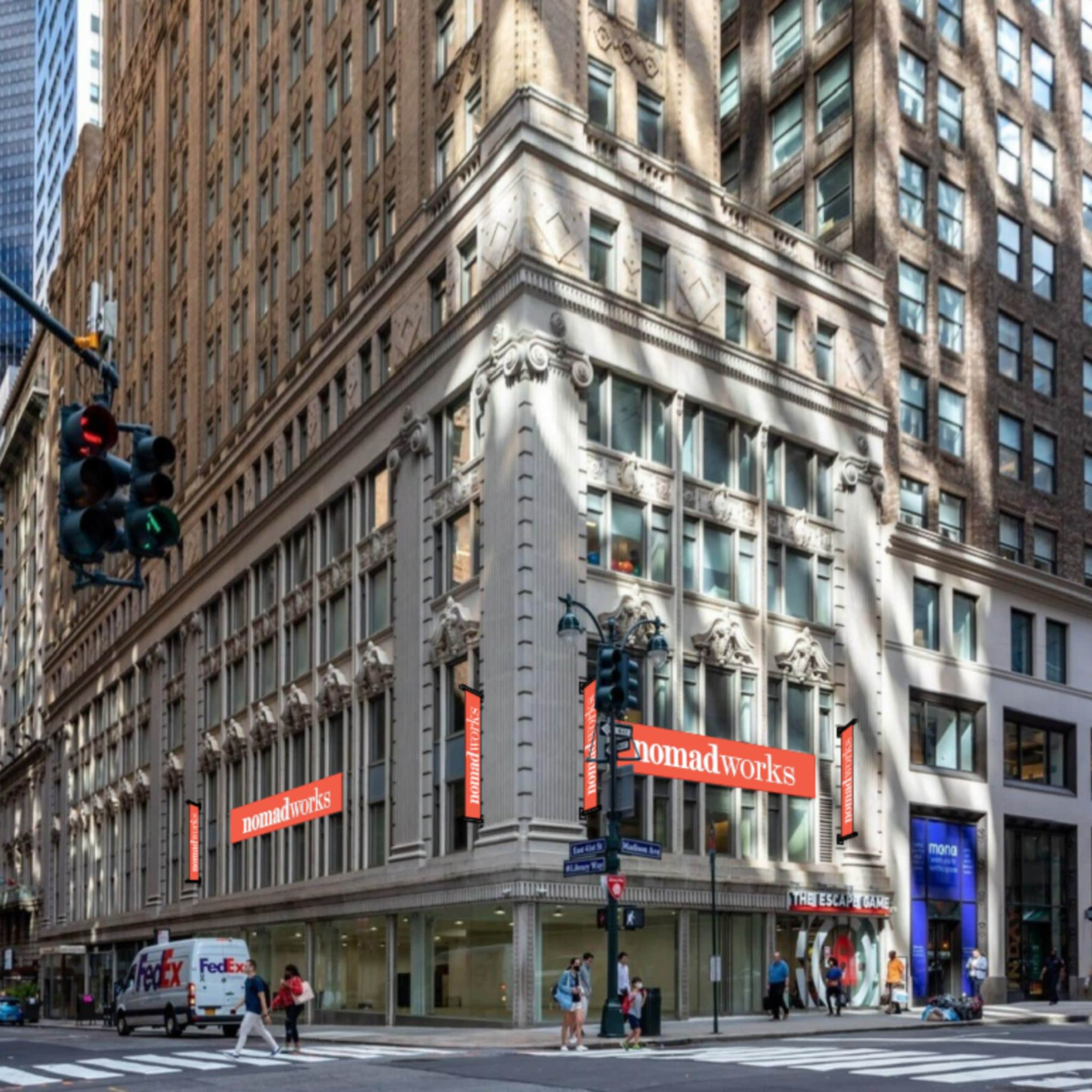 The image shows a street corner in a city, featuring an ornate building adorned with large Nomadworks banners, with pedestrians and a delivery vehicle nearby.