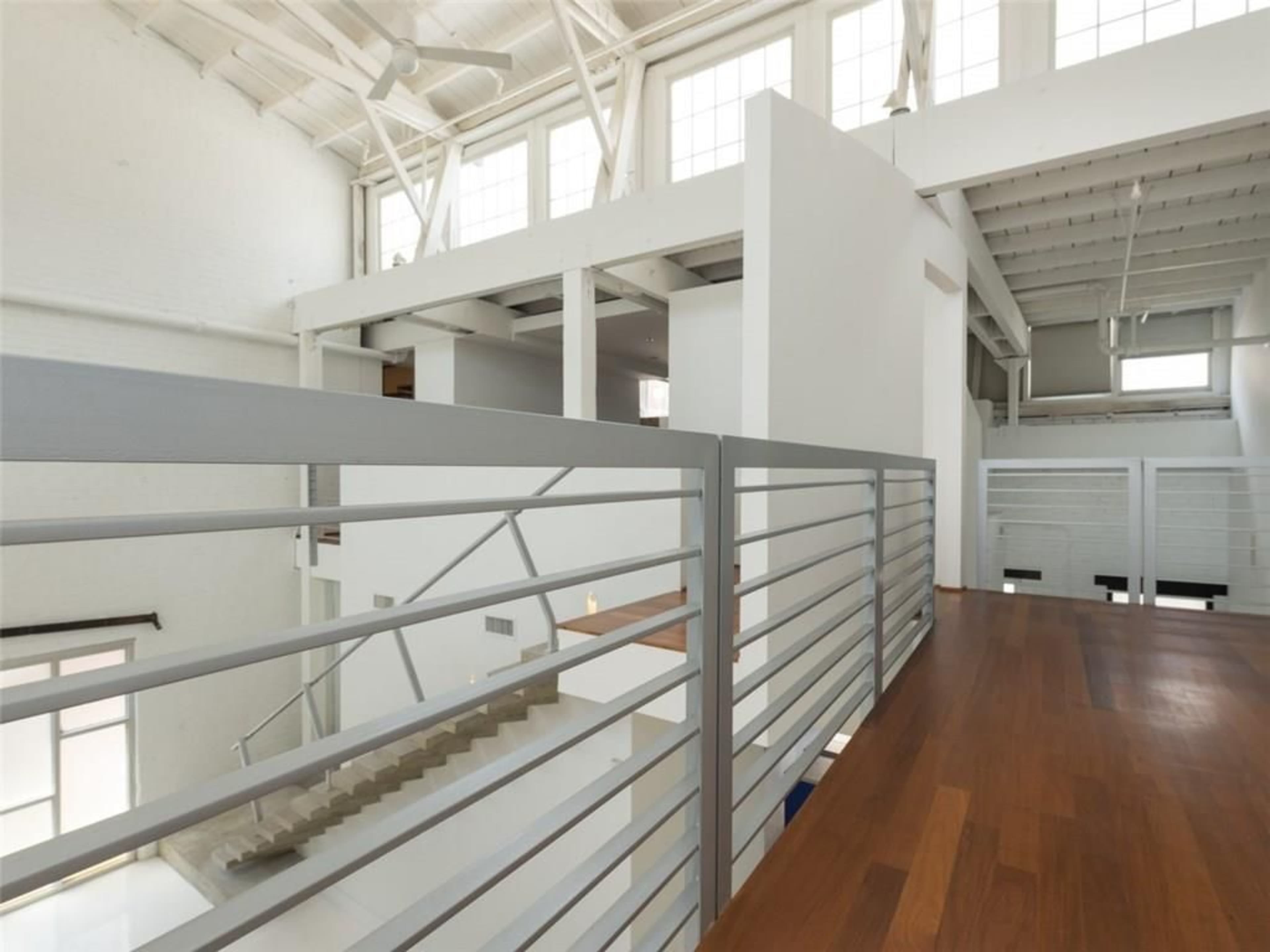 A modern interior space with a wooden balcony overlooking a staircase and open floor plan beneath.
