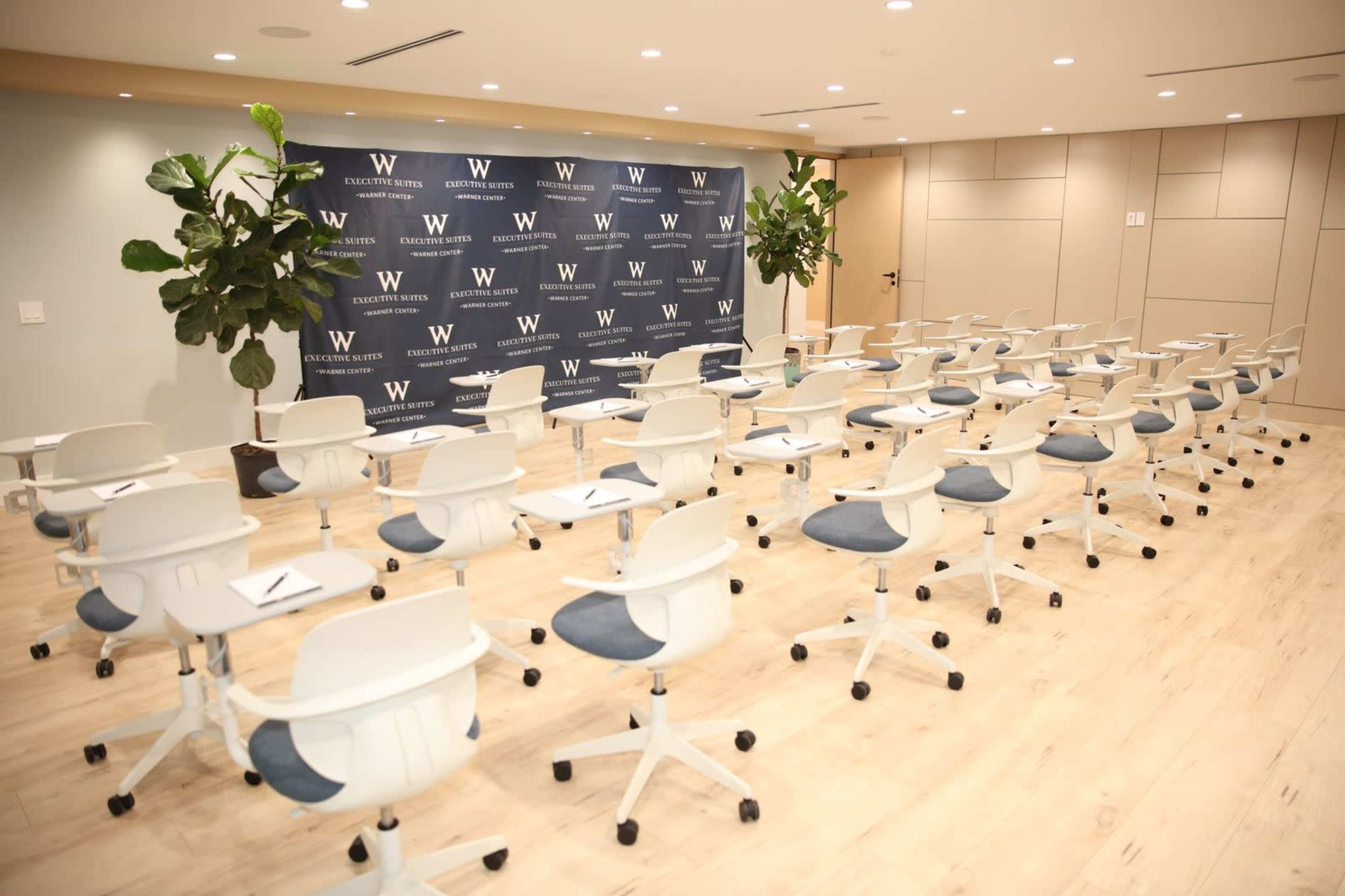 The image shows a seminar room arranged with rows of white chairs and a backdrop featuring the letter "W" and the text "ELECTRIC BEACH."