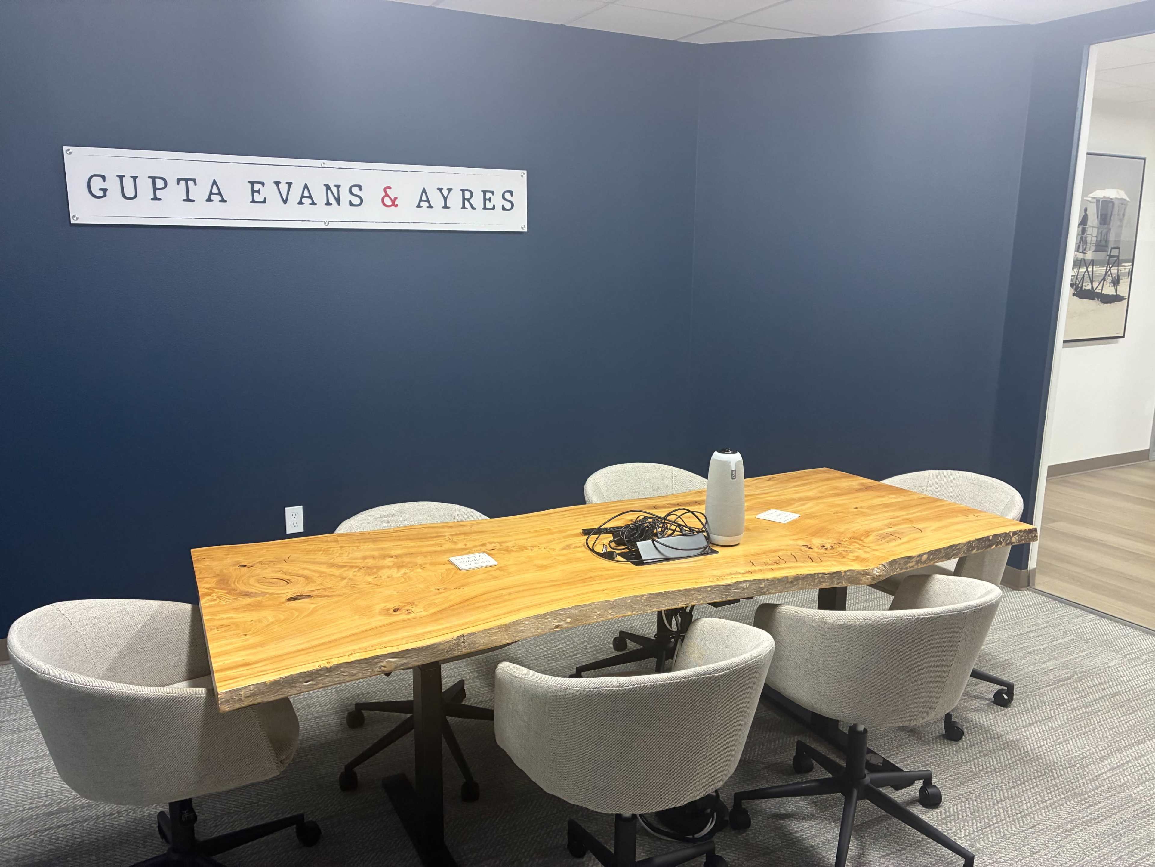 A conference room features a large wooden table surrounded by four upholstered chairs, with a wall sign that reads "GUPTA EVANS & AYRES."