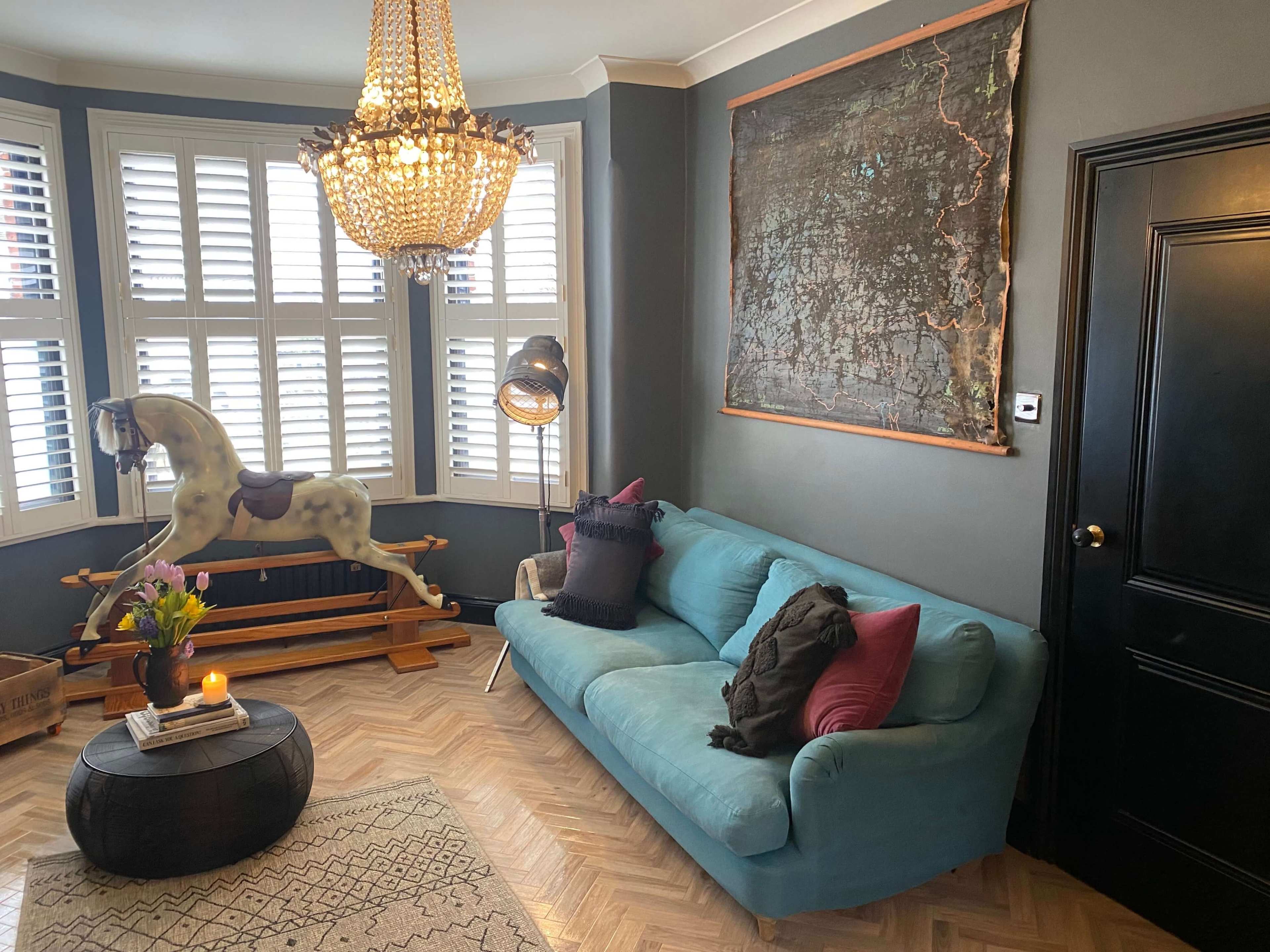 A living room with a blue sofa, a wooden rocking horse, a large map on the wall, and a chandelier overhead, along with a round black coffee table and decorative pillows.