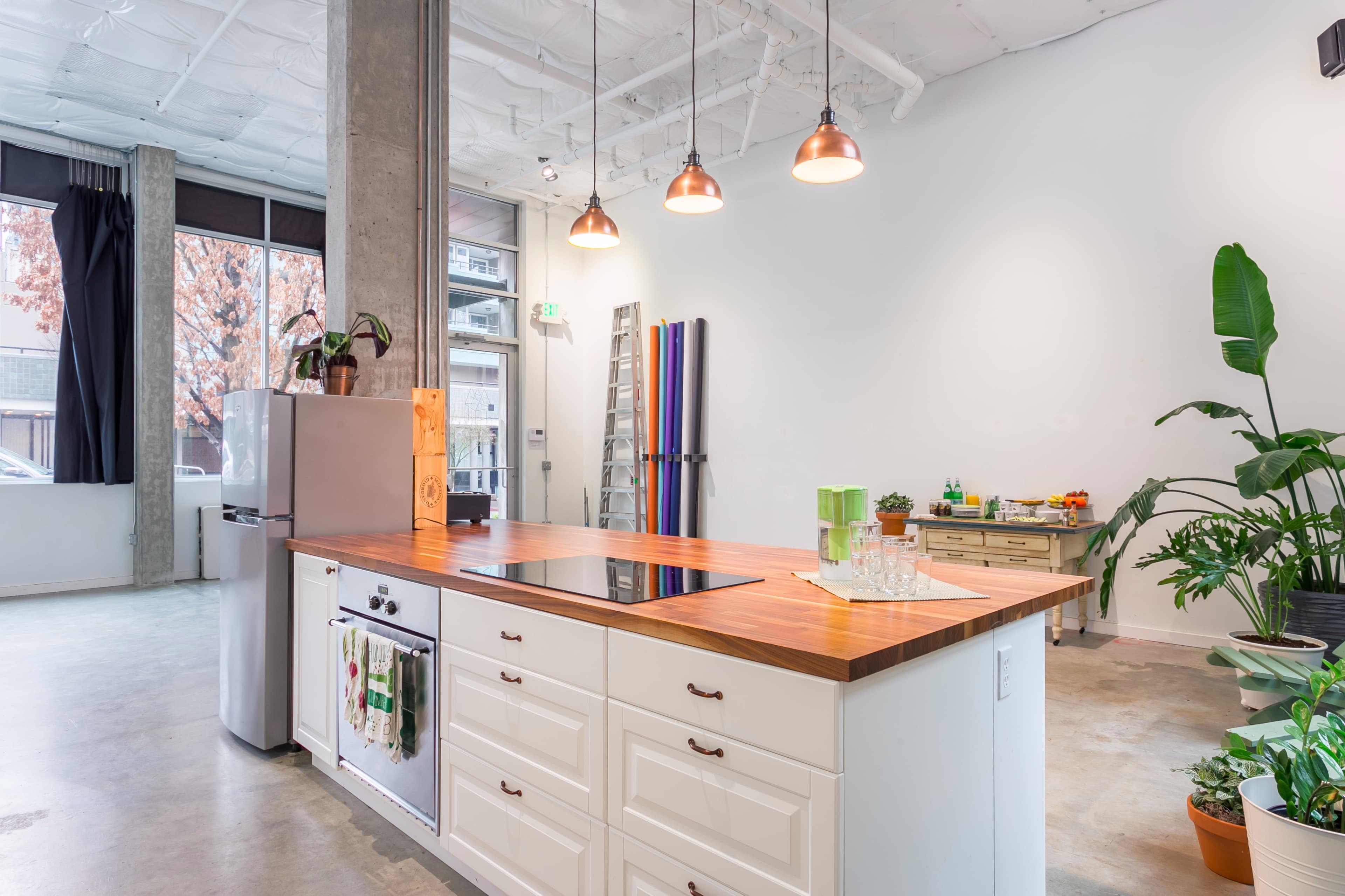 A modern kitchen with a wooden island, white cabinetry, stainless steel appliances, and various potted plants.