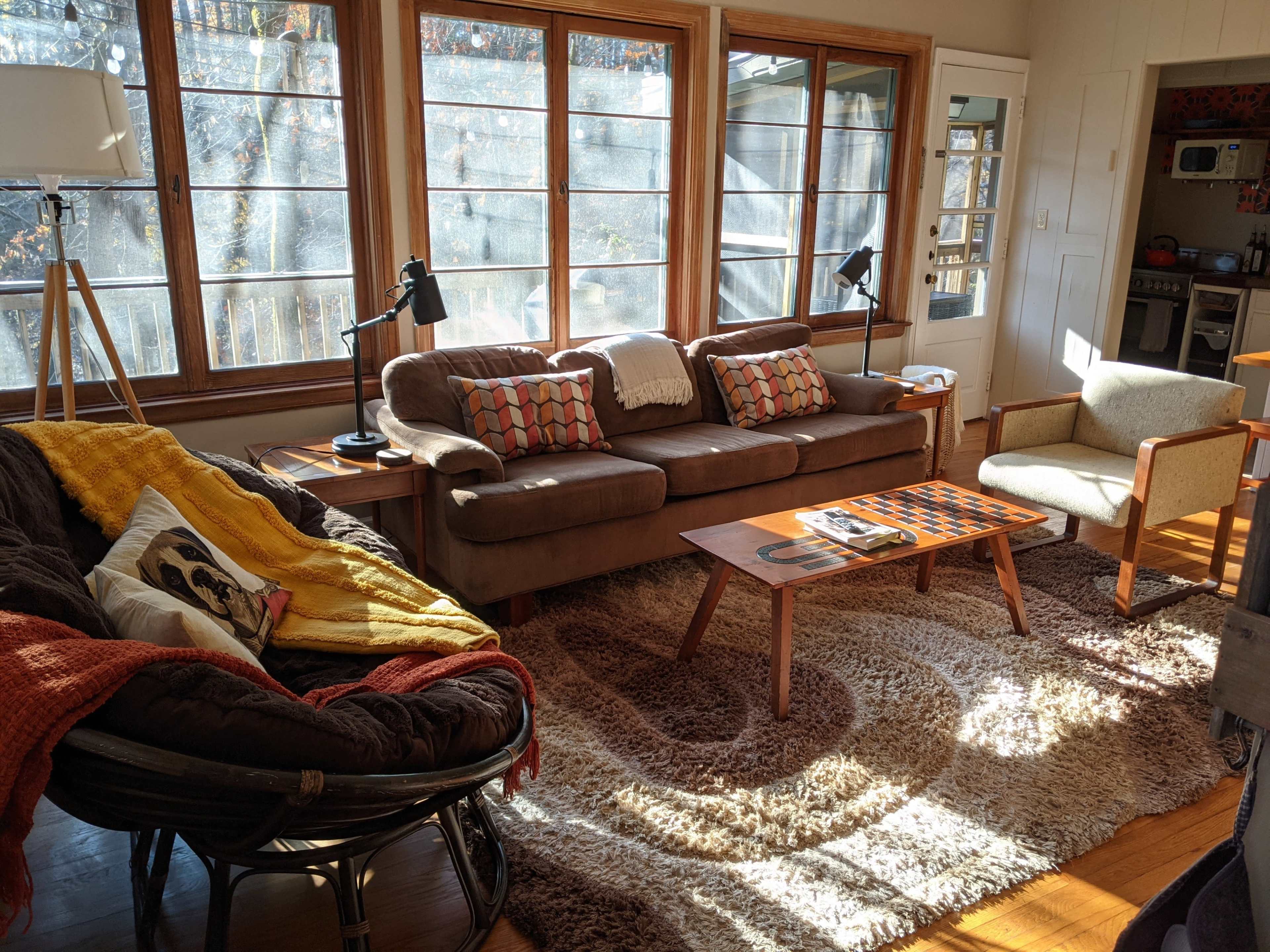 The living room features a sofa, an armchair, a coffee table with a checkerboard, and large windows allowing natural light.