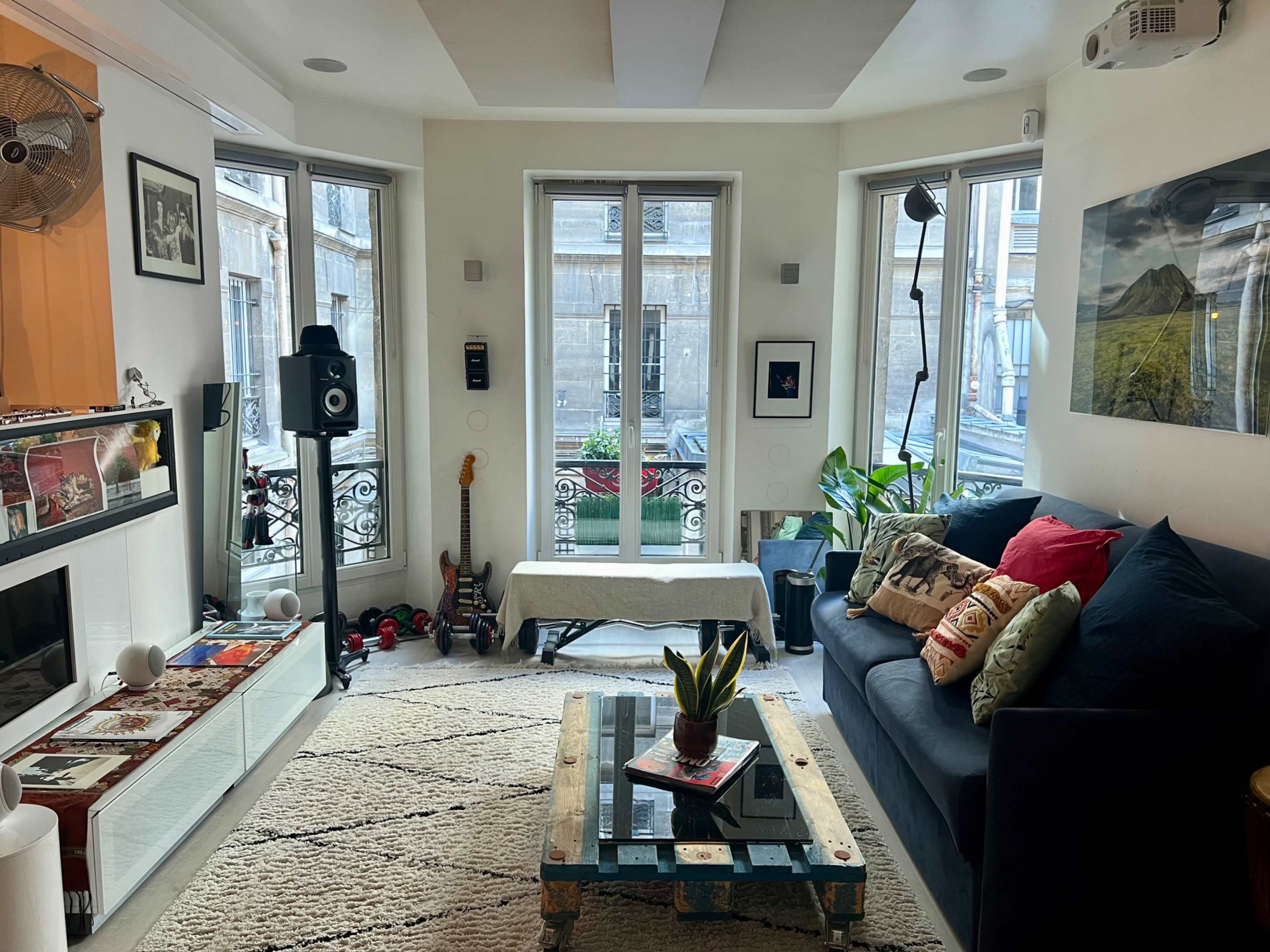 The living room features a couch, a coffee table, a guitar, and large windows that overlook an external balcony.