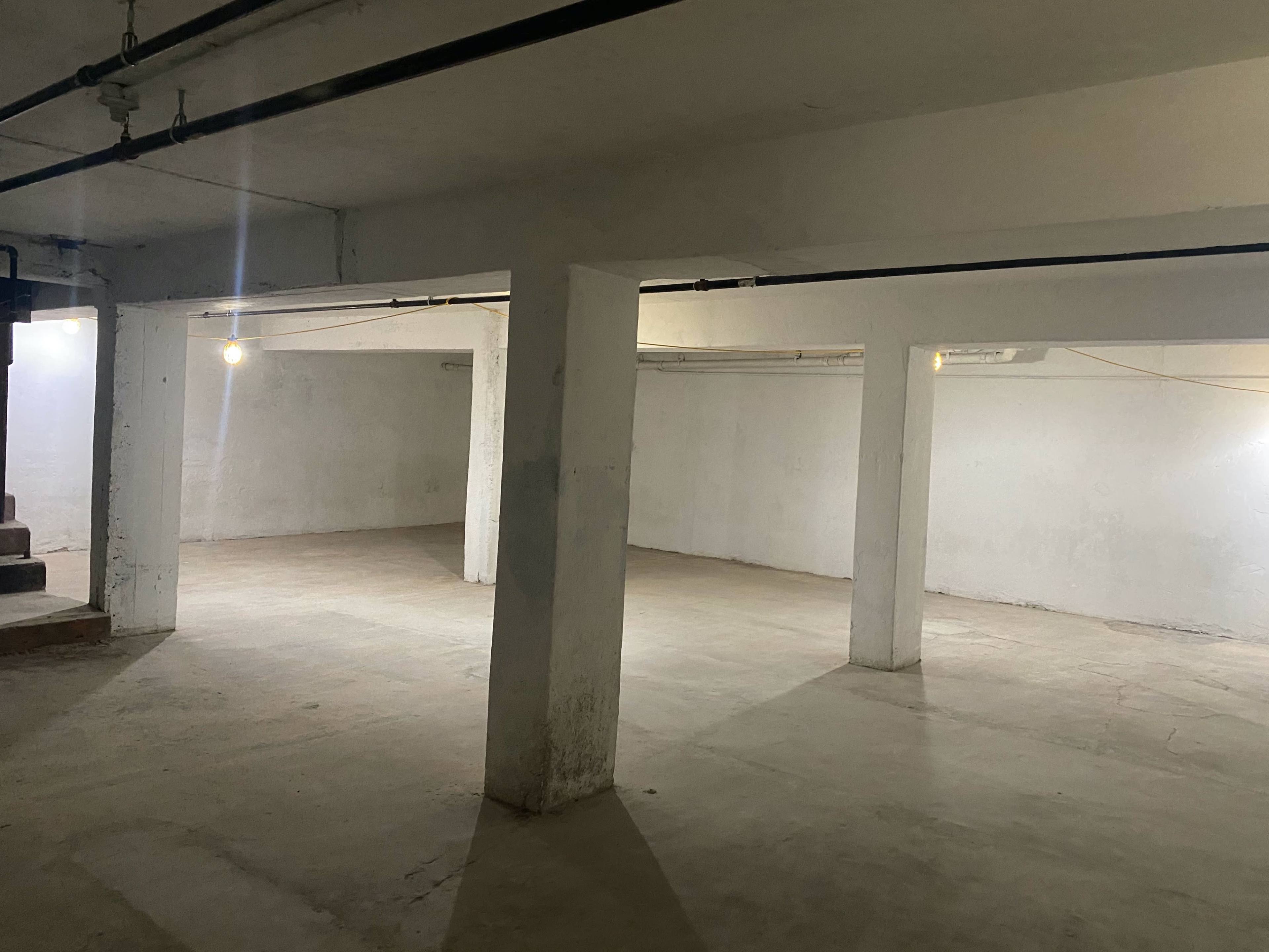 A large, empty basement with concrete floors, white walls, and several overhead lights illuminating the space.