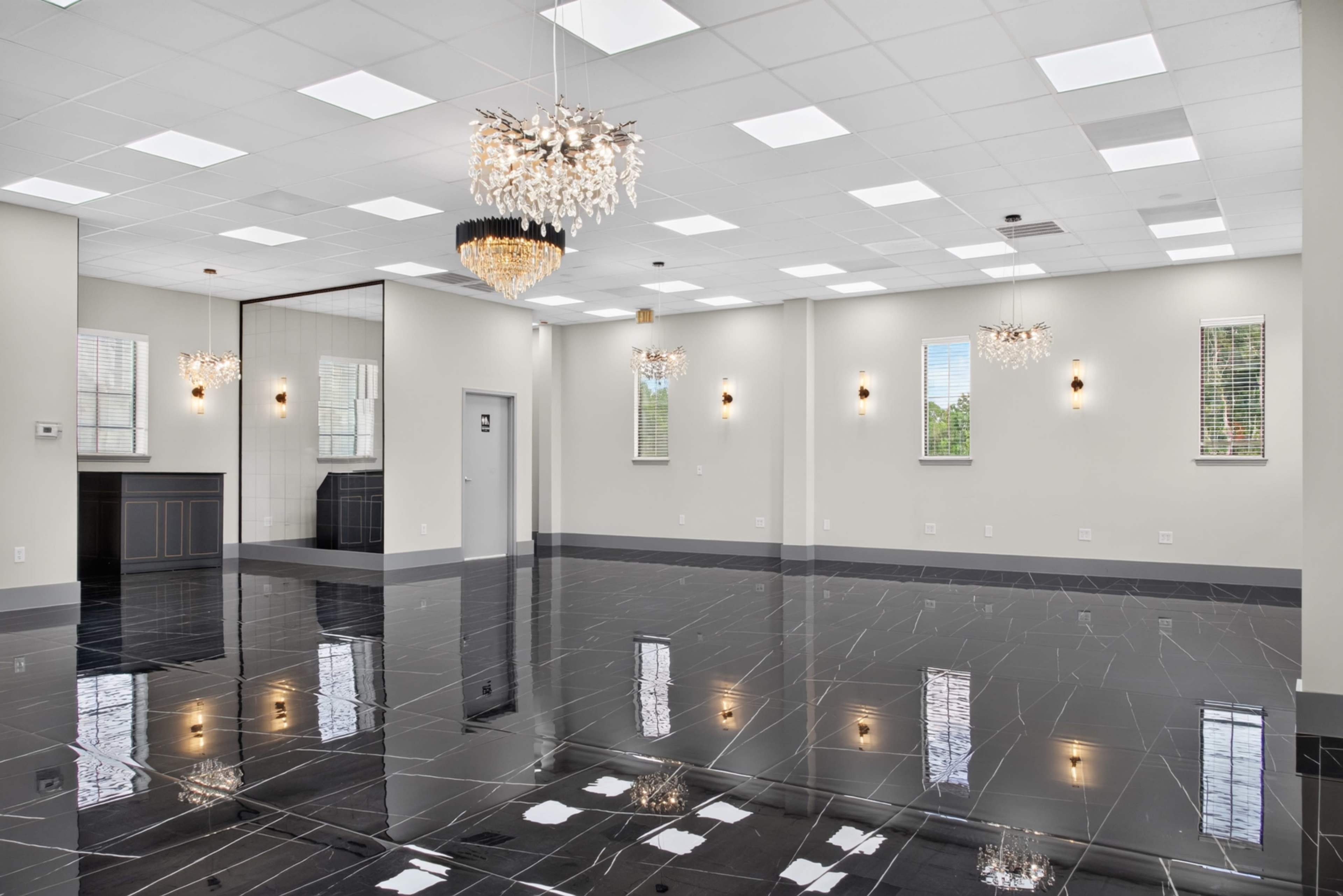 The image shows an elegantly designed room with glossy black tile flooring, bright ceiling lights, and modern chandeliers.