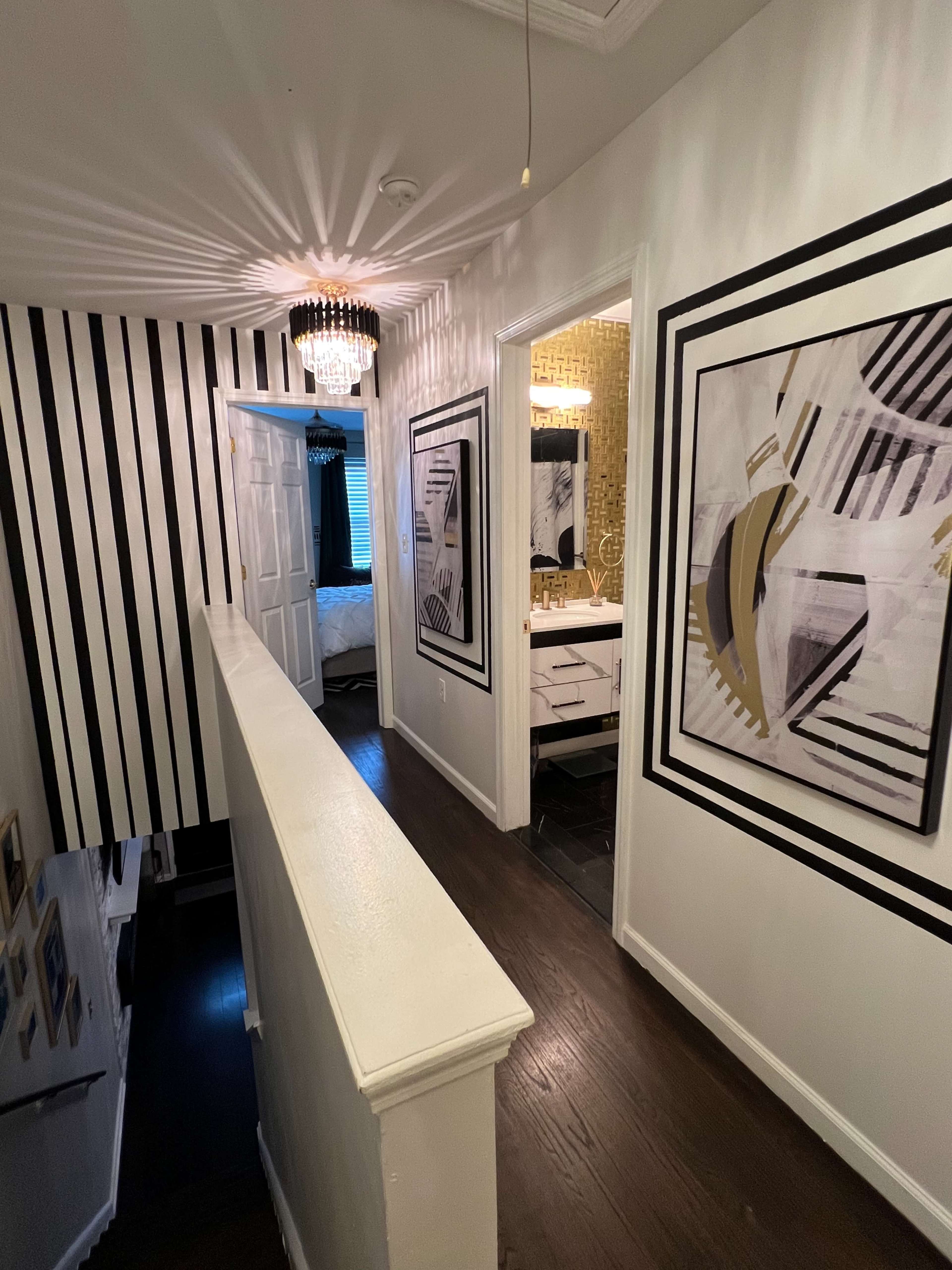 A hallway with black and white striped walls, framed artwork, and a ceiling light fixture.