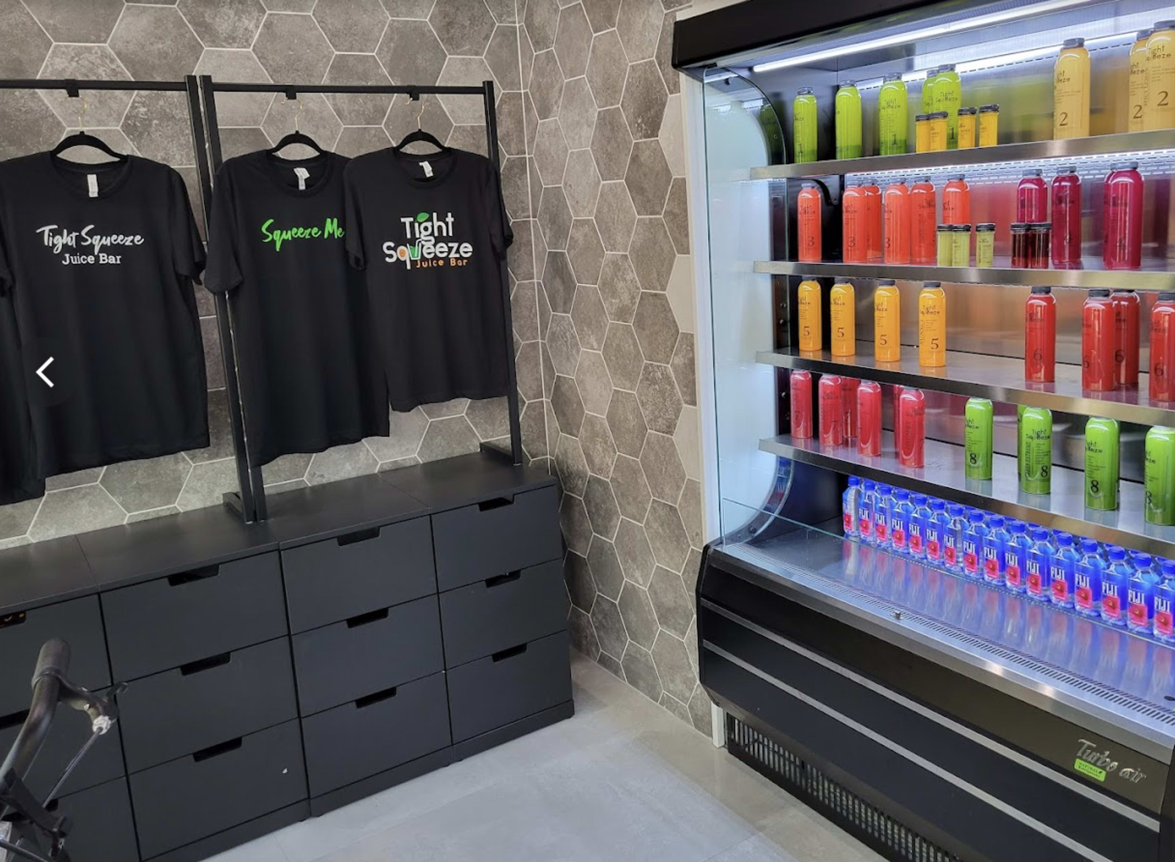 The image shows a juice bar with a display of brightly colored beverage cans and black T-shirts hanging on a rack.