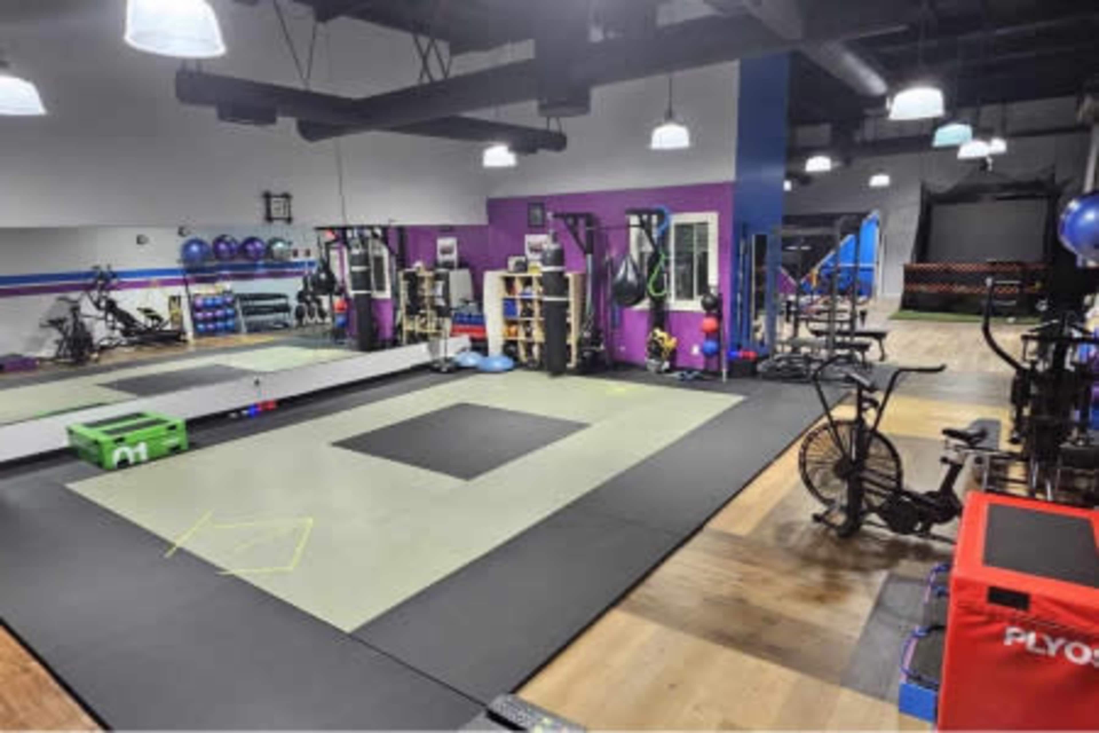 The image shows a well-equipped gym space featuring exercise mats, gym equipment, and cardio machines in a spacious layout.