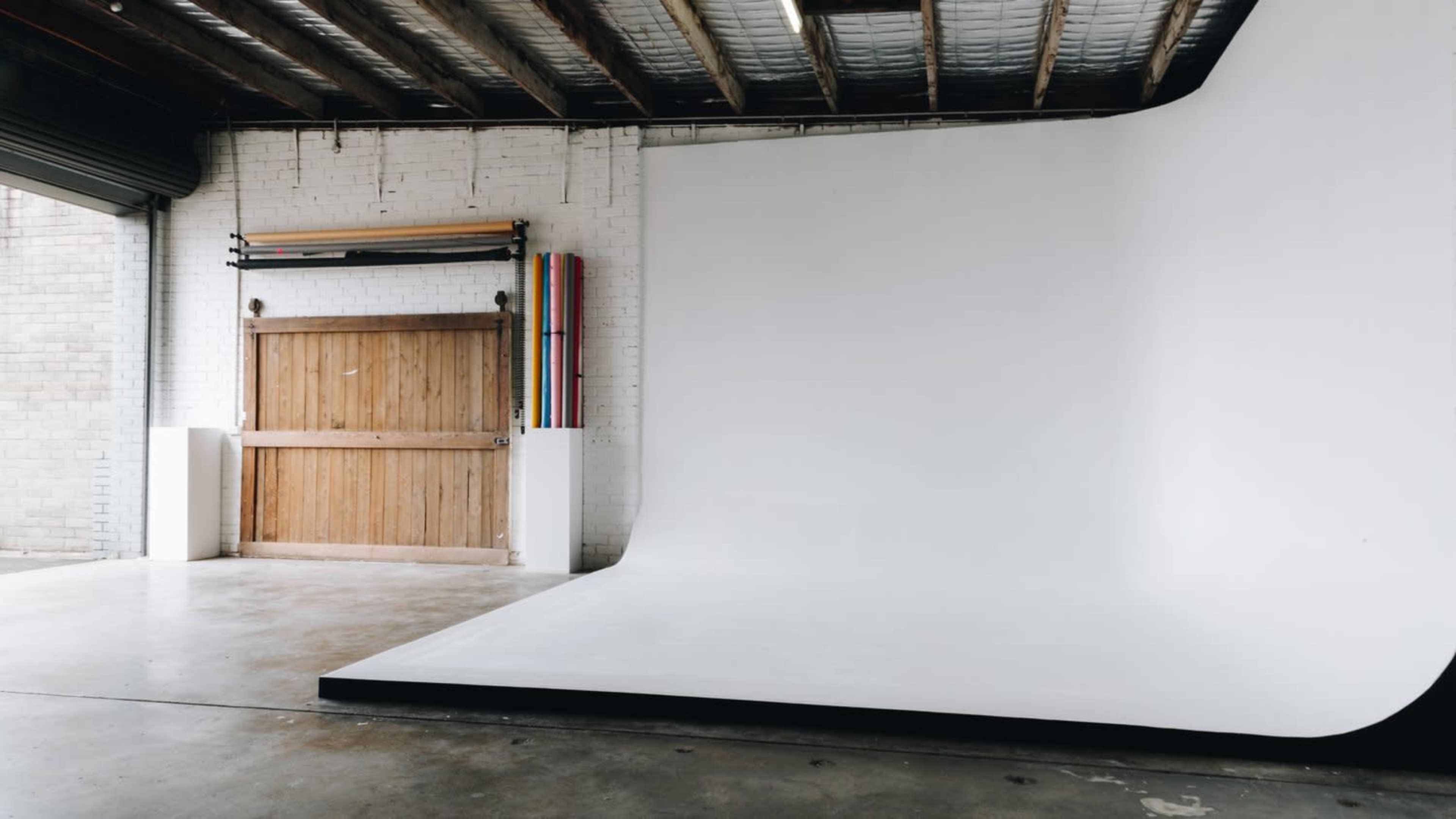 A spacious photo studio with a wide, seamless white backdrop and wooden double doors in the background.