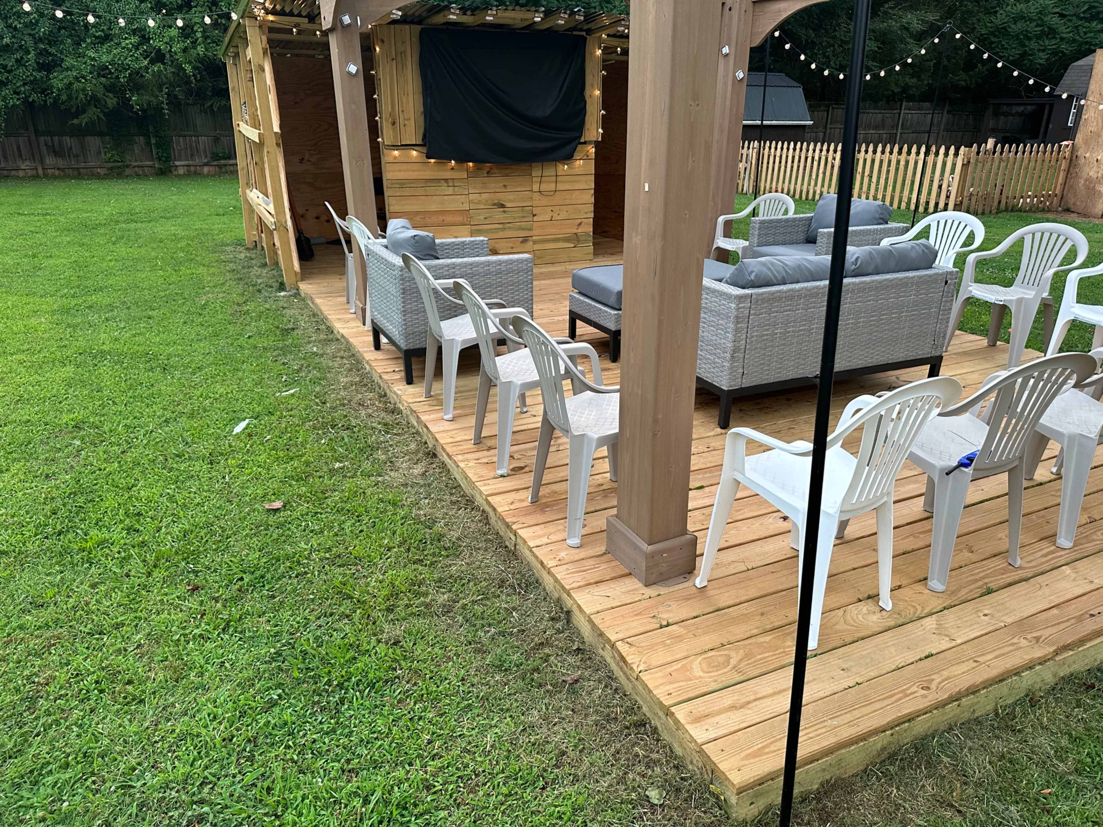 A wooden deck area with a few gray couches and multiple white chairs arranged around a patio space.