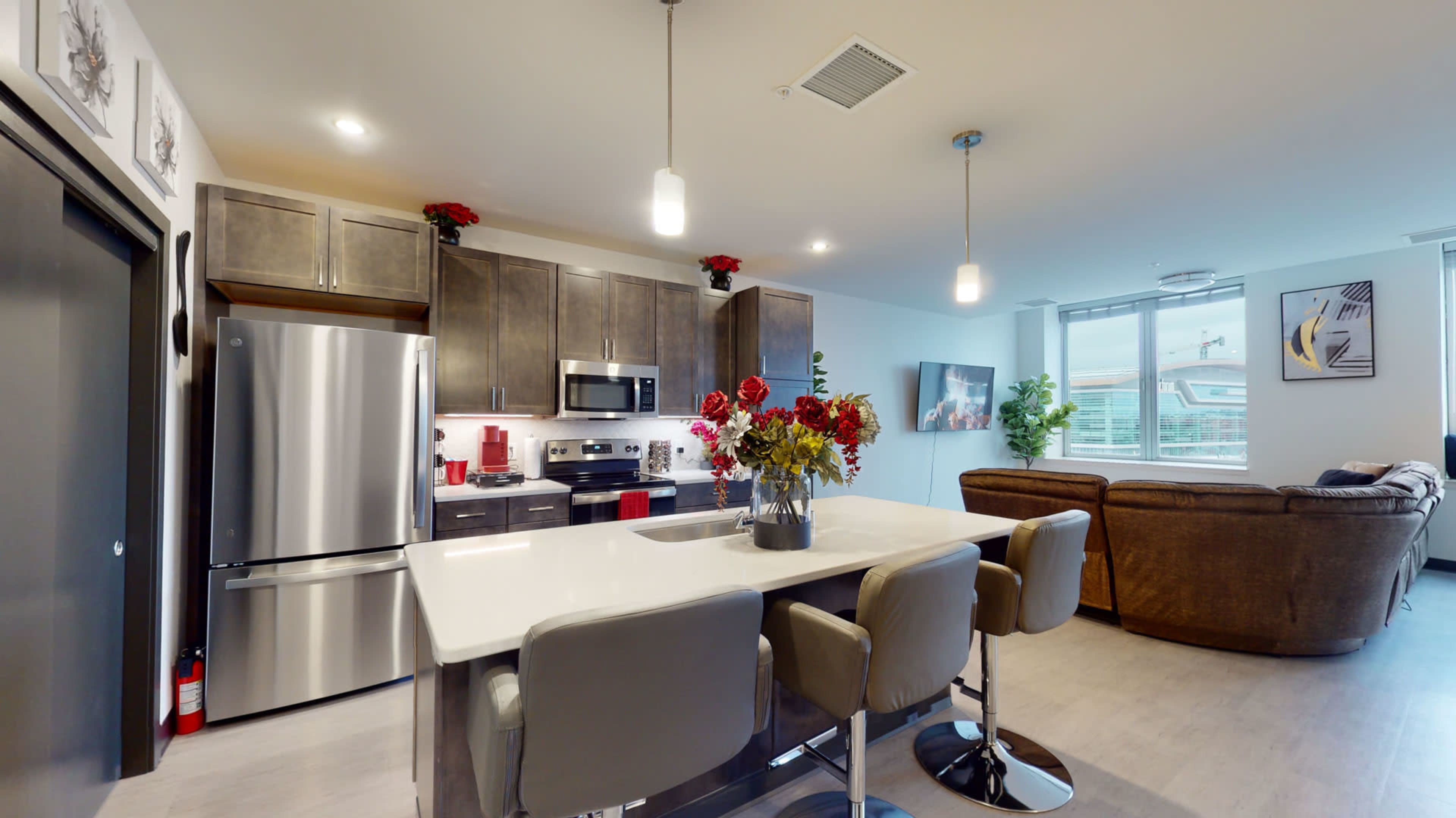 A modern kitchen with stainless steel appliances, a large island with seating, and a living area featuring a couch and decorative plants.
