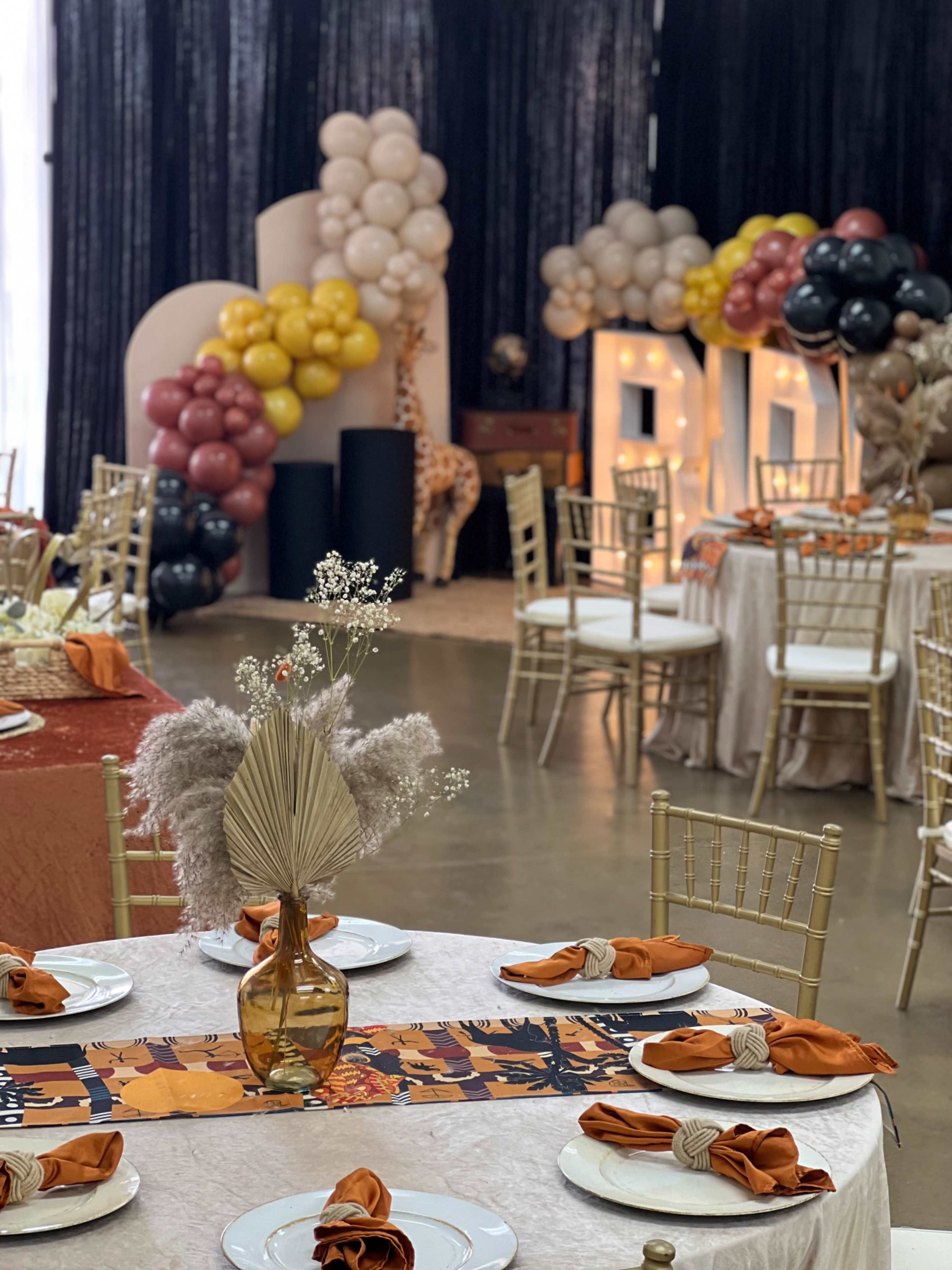 A decorated event space with tables set for dining, featuring elegant centerpieces and a backdrop of balloons and illuminated letters.