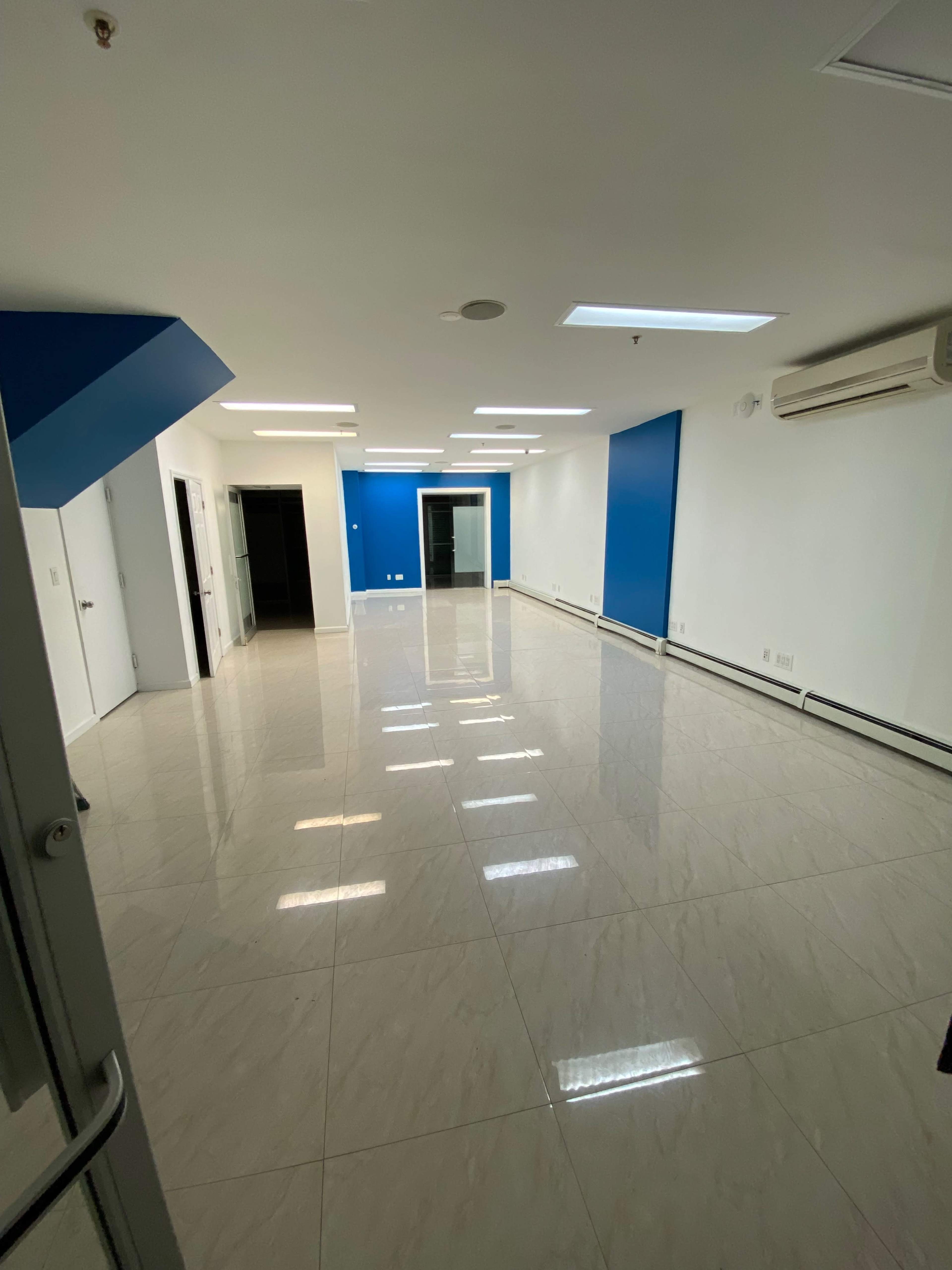 A spacious, empty office room with white walls, blue accent walls, and shiny tiled flooring.