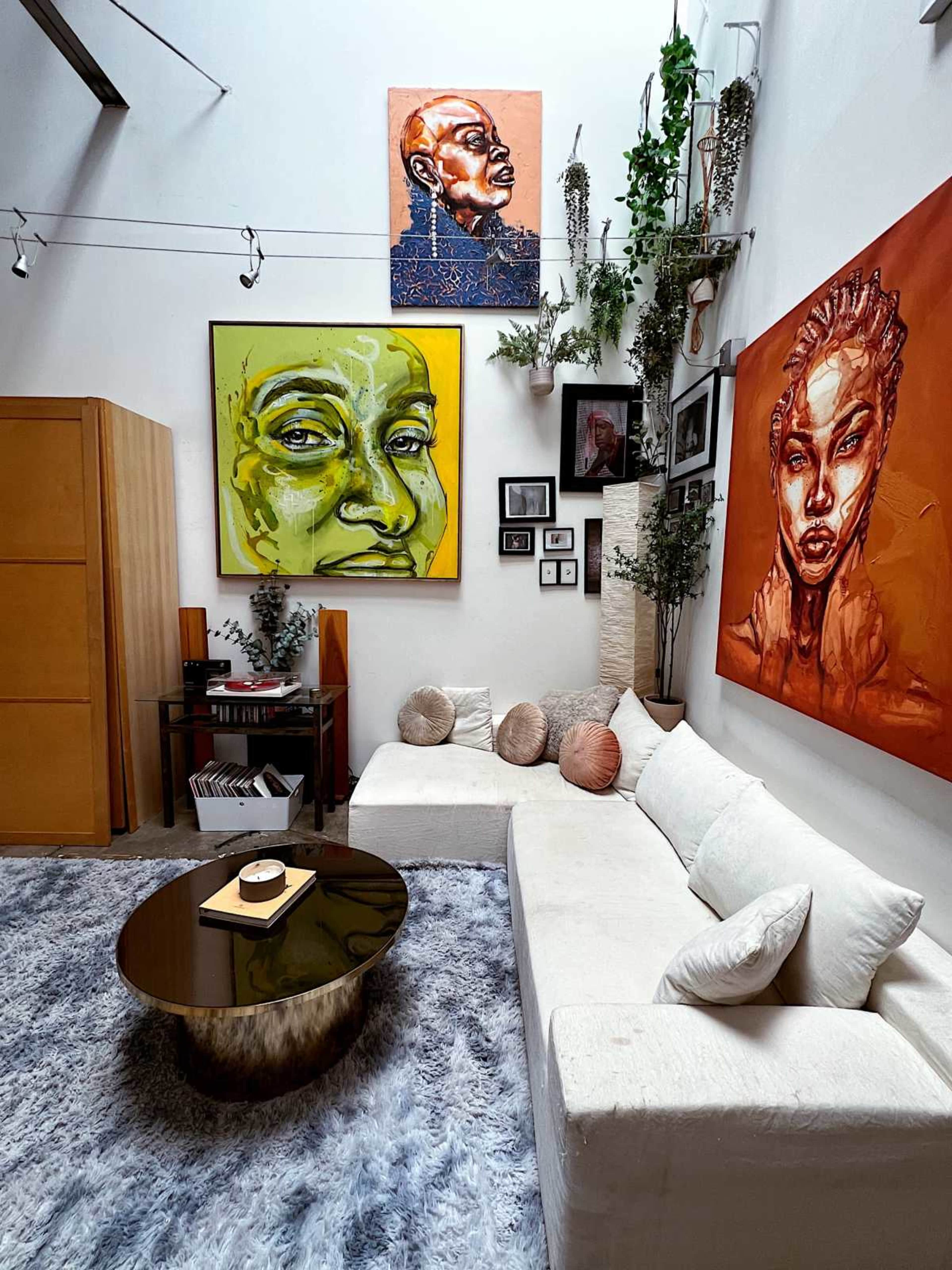 The image shows a modern, minimalist living room featuring a large white sectional sofa, a round coffee table, and vibrant artwork on the walls.