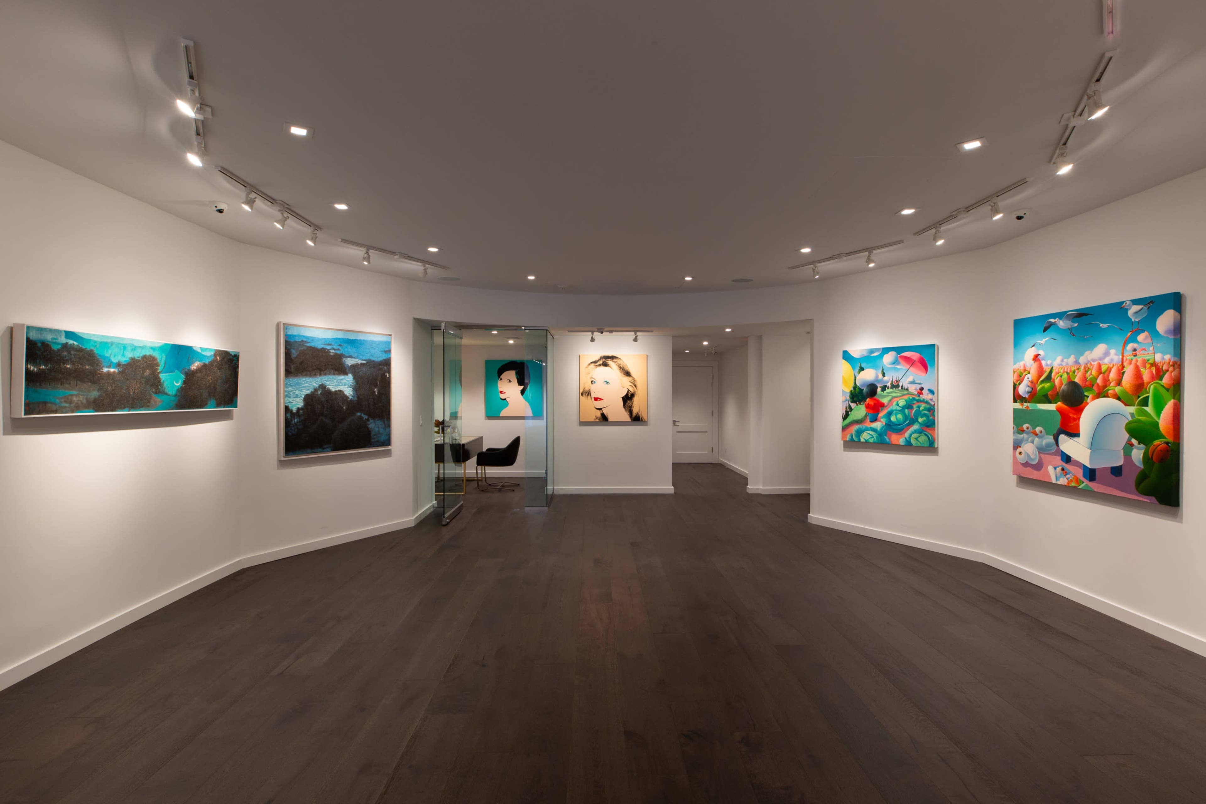 The image shows an art gallery with various colorful artworks displayed on the walls, featuring a circular layout and wooden flooring.